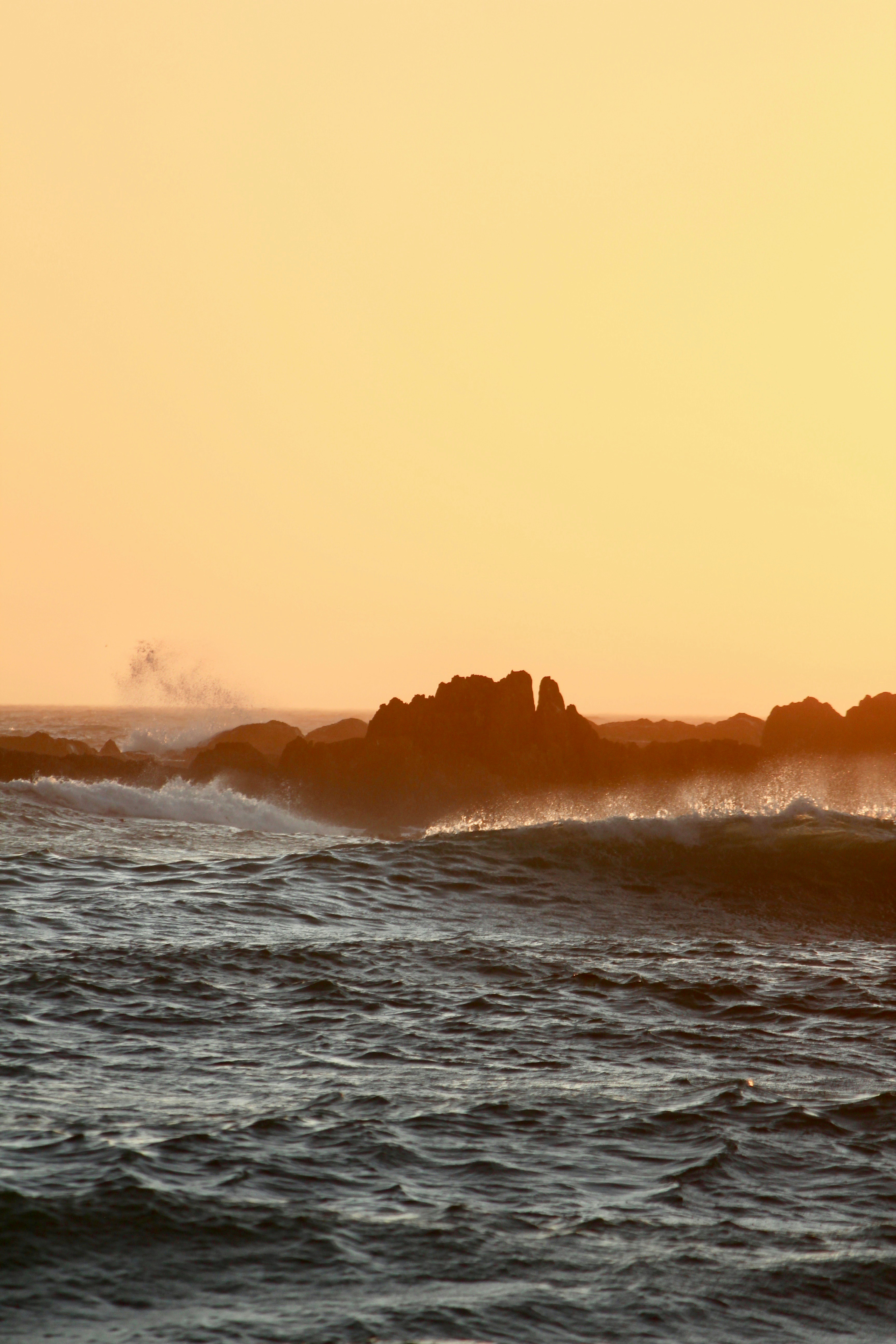Waves crash against rocks at sunset.
