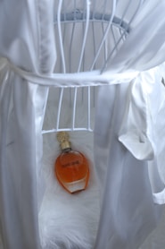 Perfume and a white robe on a fluffy surface.