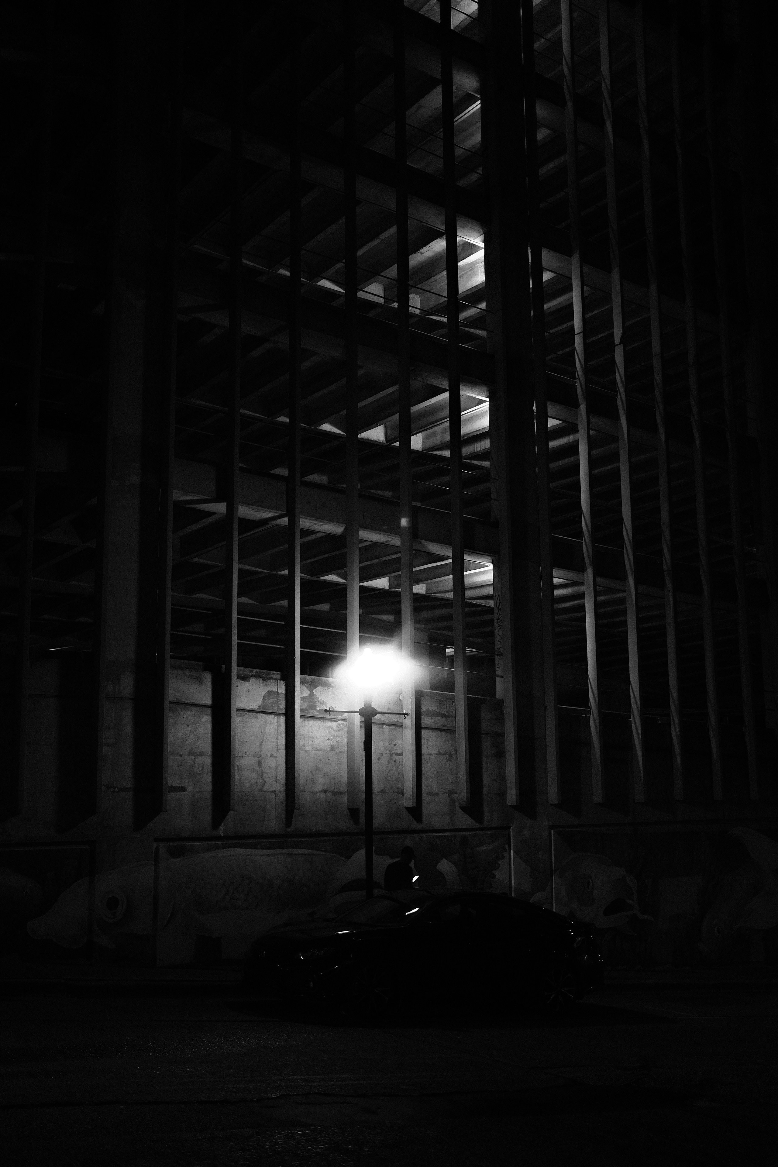 A car sits under a dark, gridded building. photo – Free Image on Unsplash