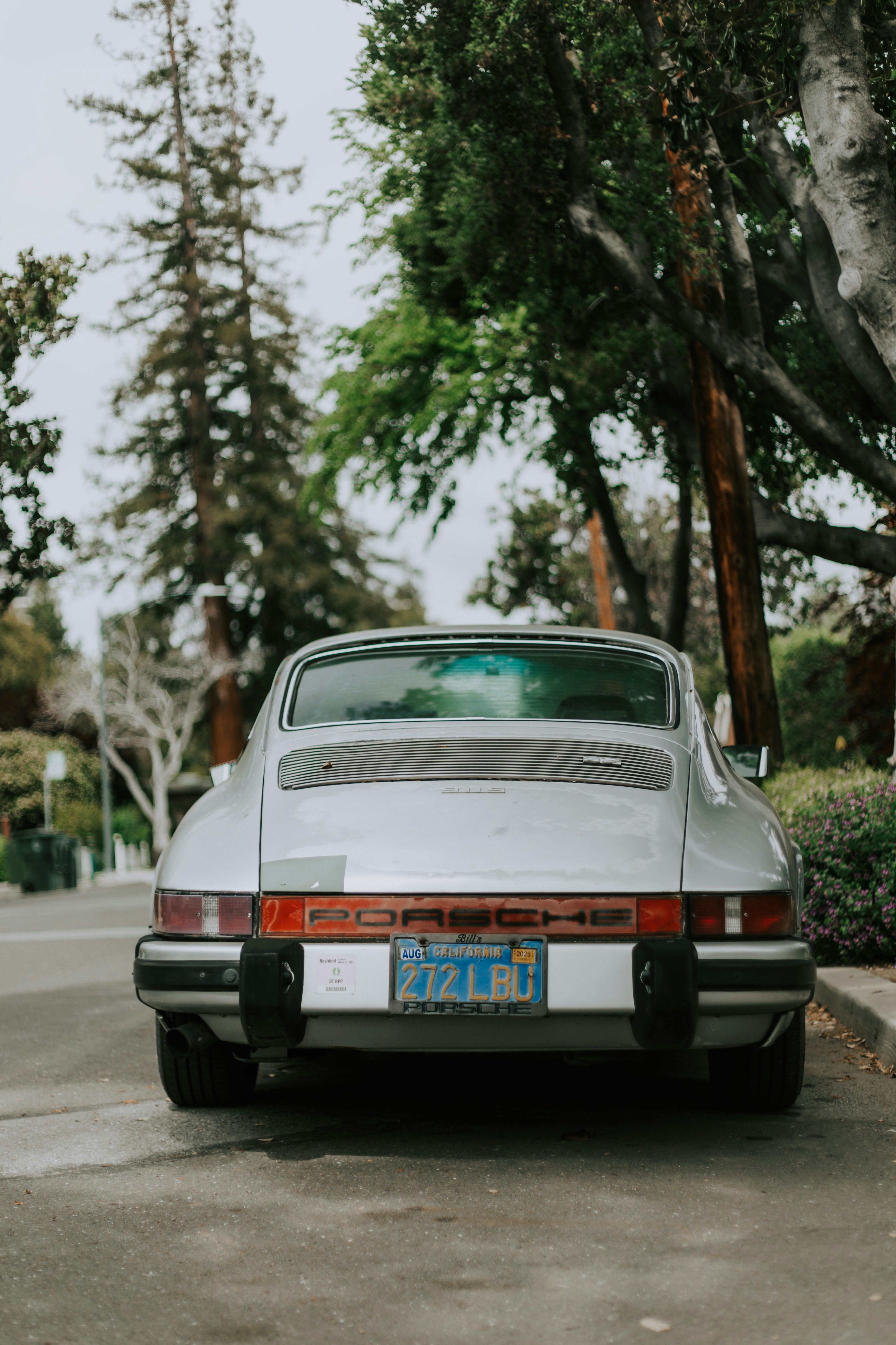 A classic silver porsche parked on the street.