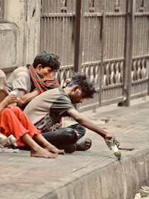 Homeless people share a bottle near a fence.