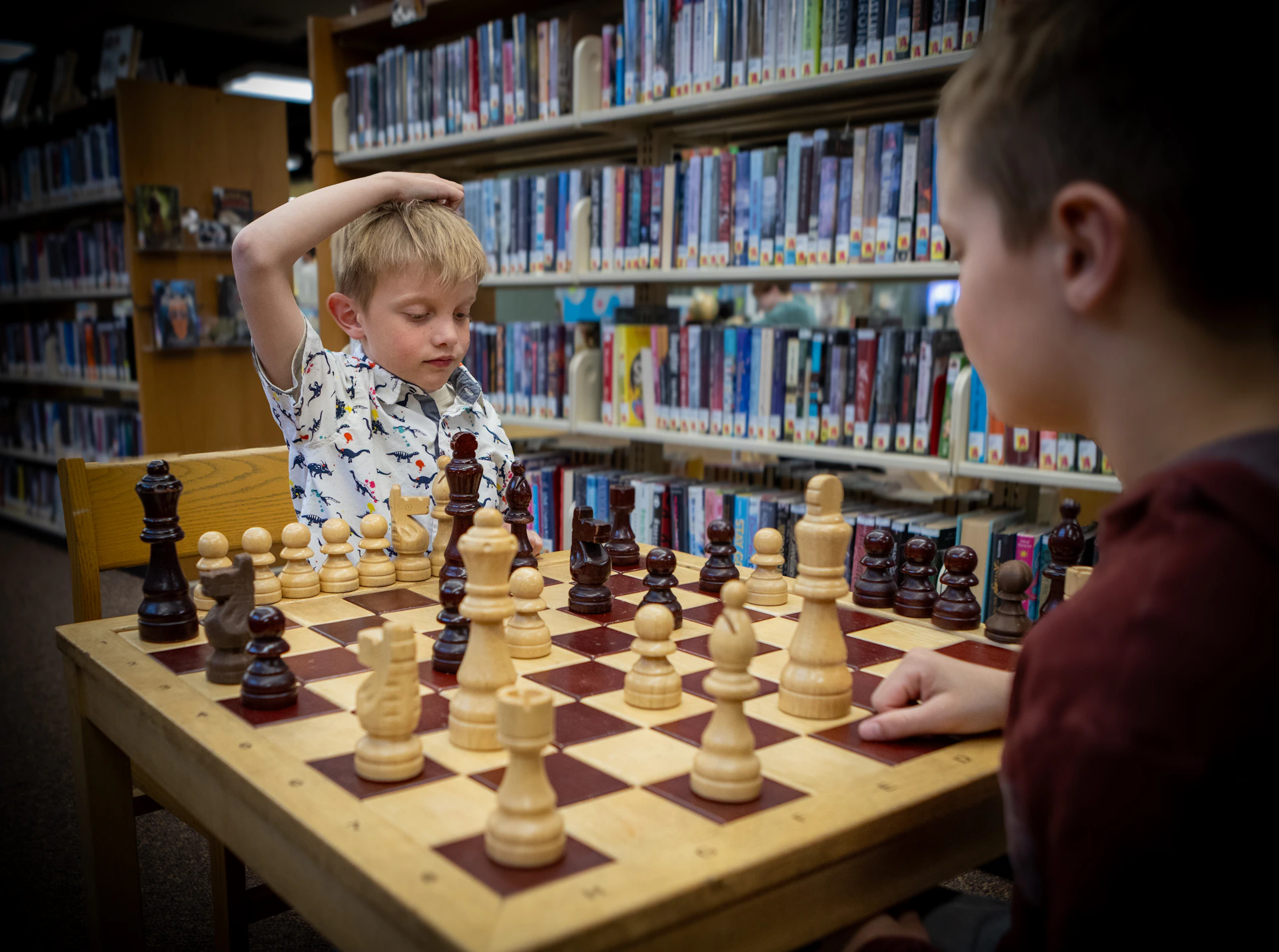 Two young boys are playing chess in a library