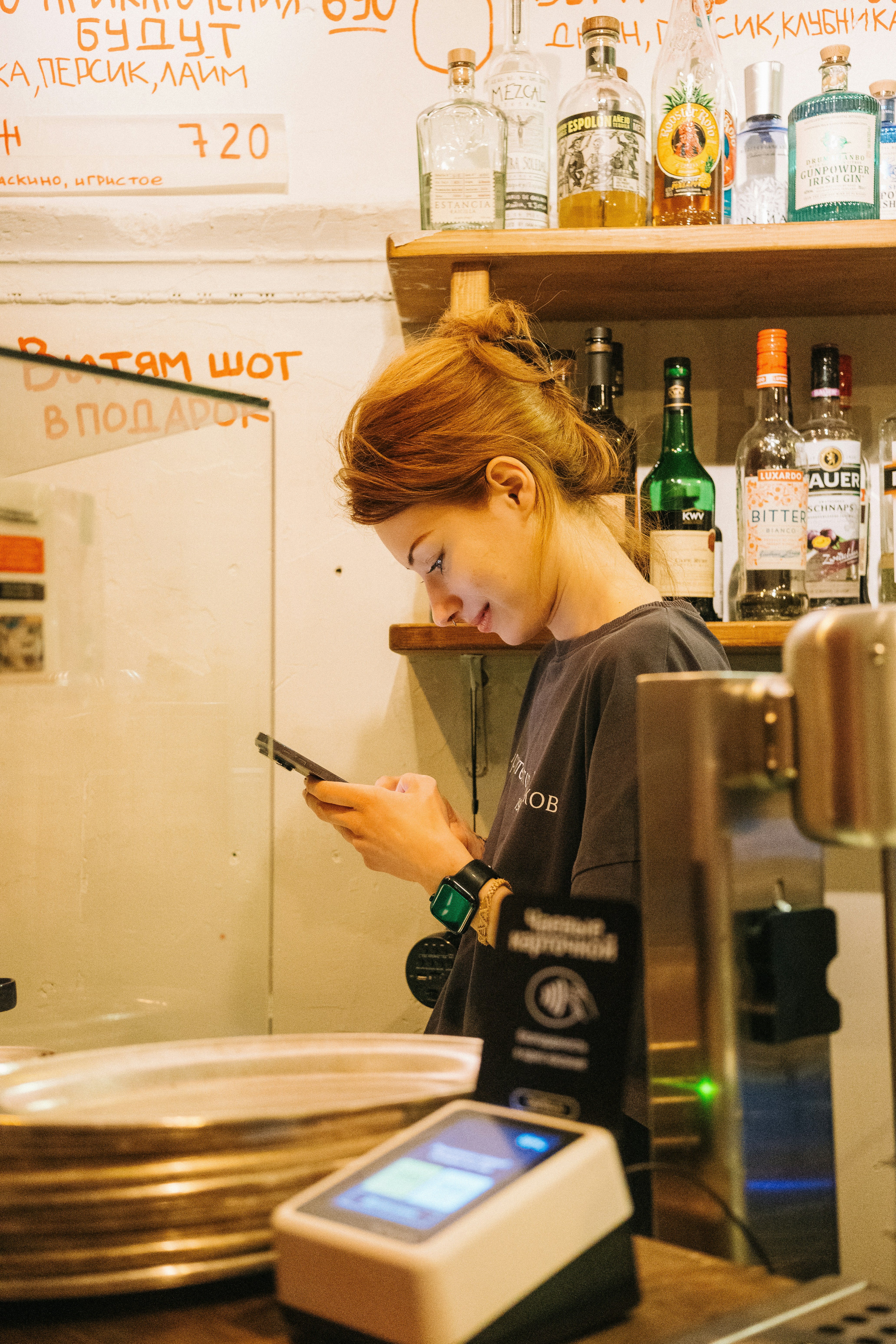 Una barista che guarda il suo smartphone mentre è dietro al bancone.