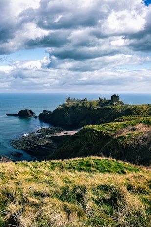 Castle ruins sit atop a rugged coastal cliff.