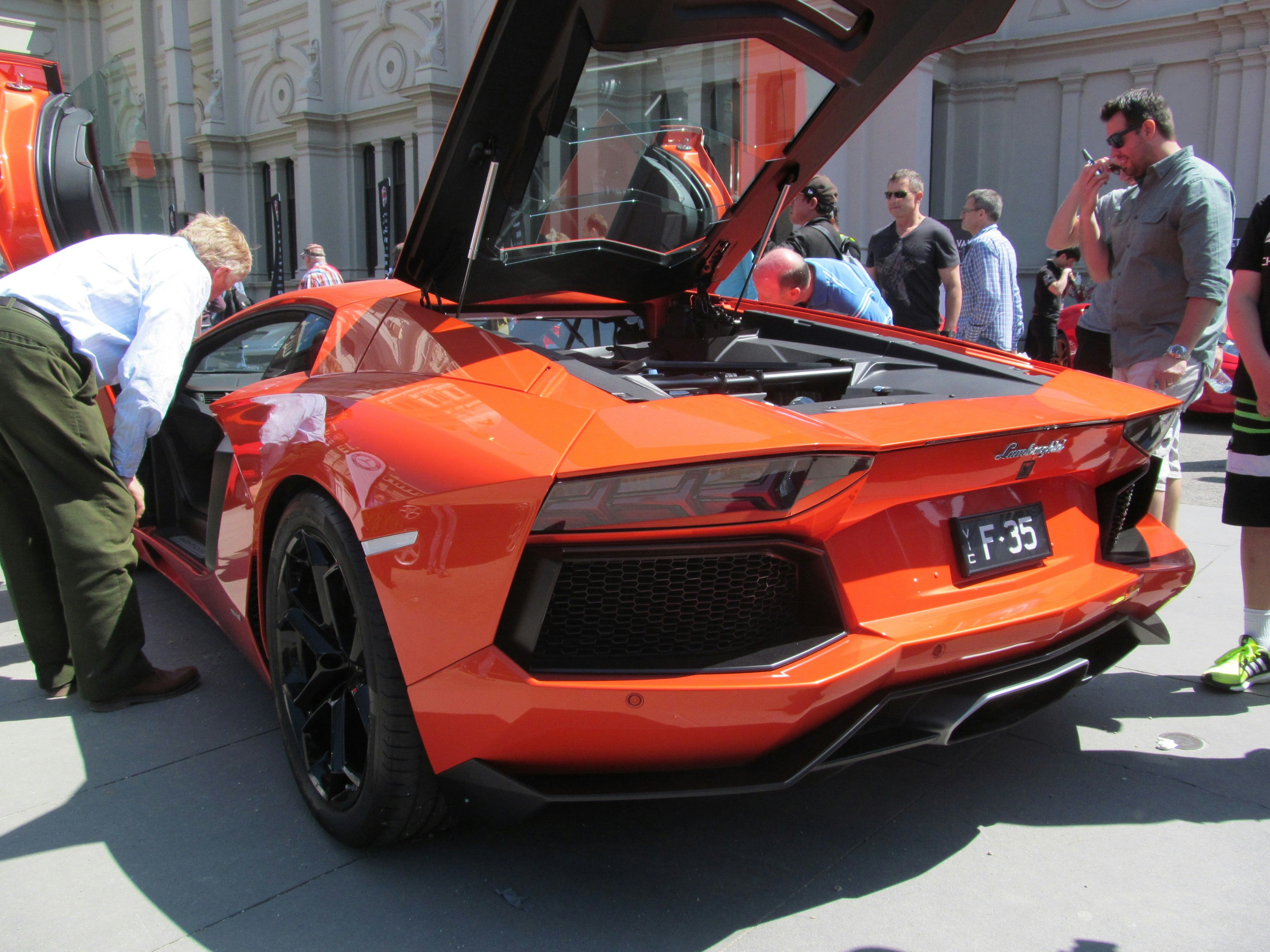People are admiring a vibrant orange lamborghini.