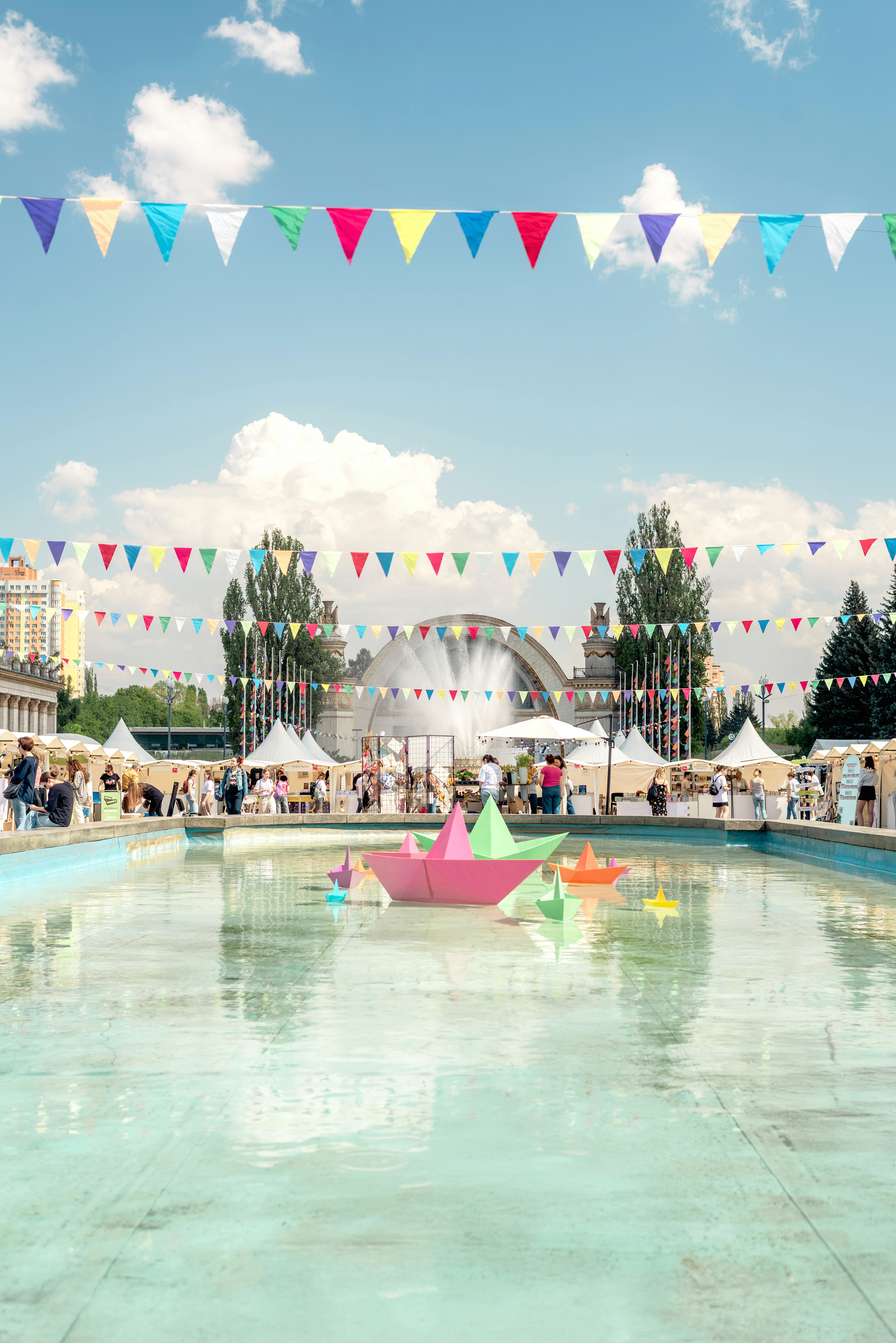 A festive outdoor market with paper boats and fountains.
