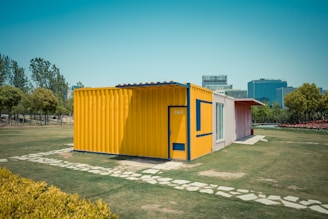 A bright yellow shipping container home on a green lawn.