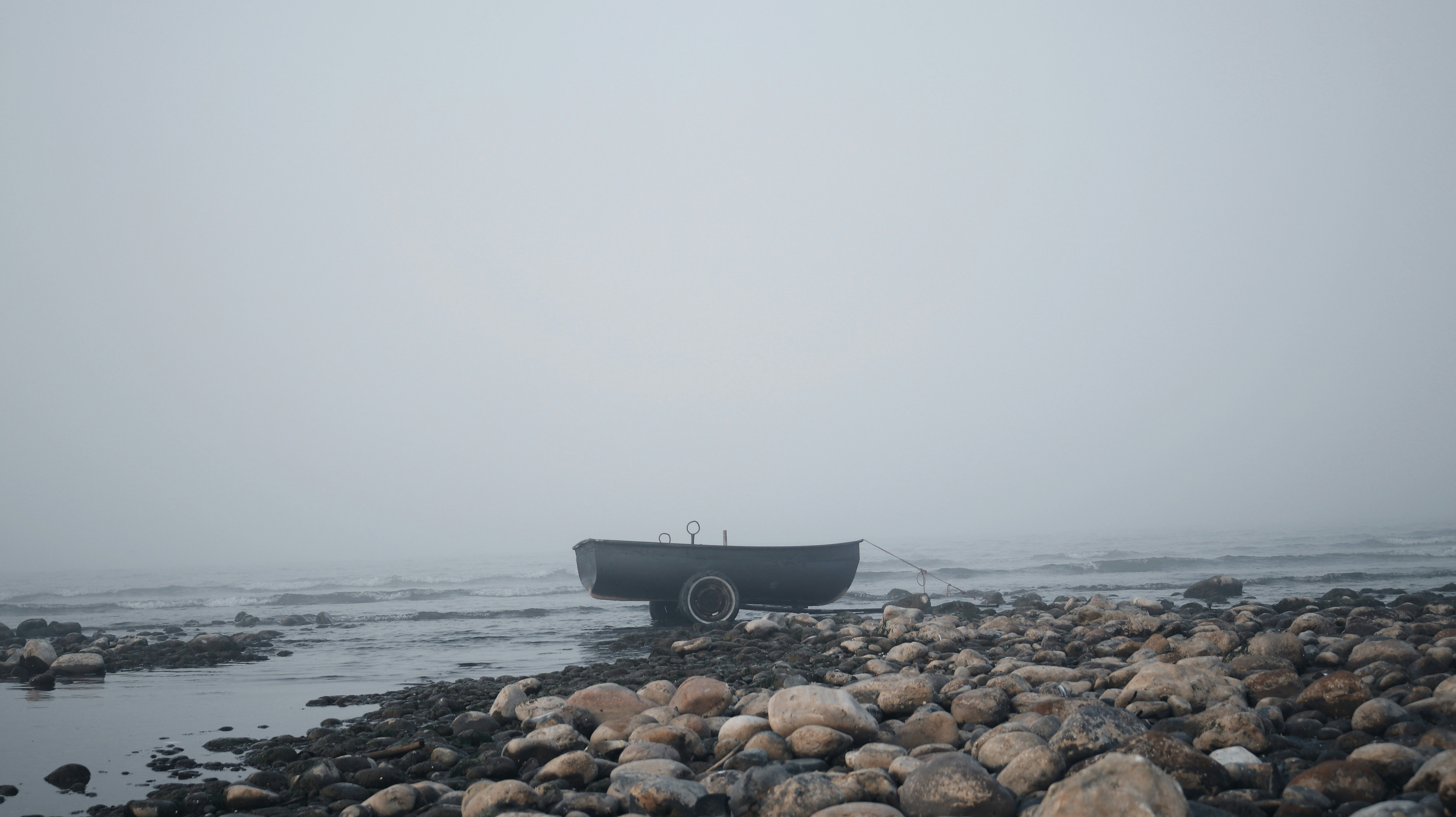 A boat sits still on the shore in the fog.