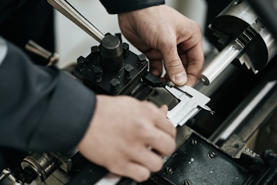 A worker measures a metal rod with calipers.