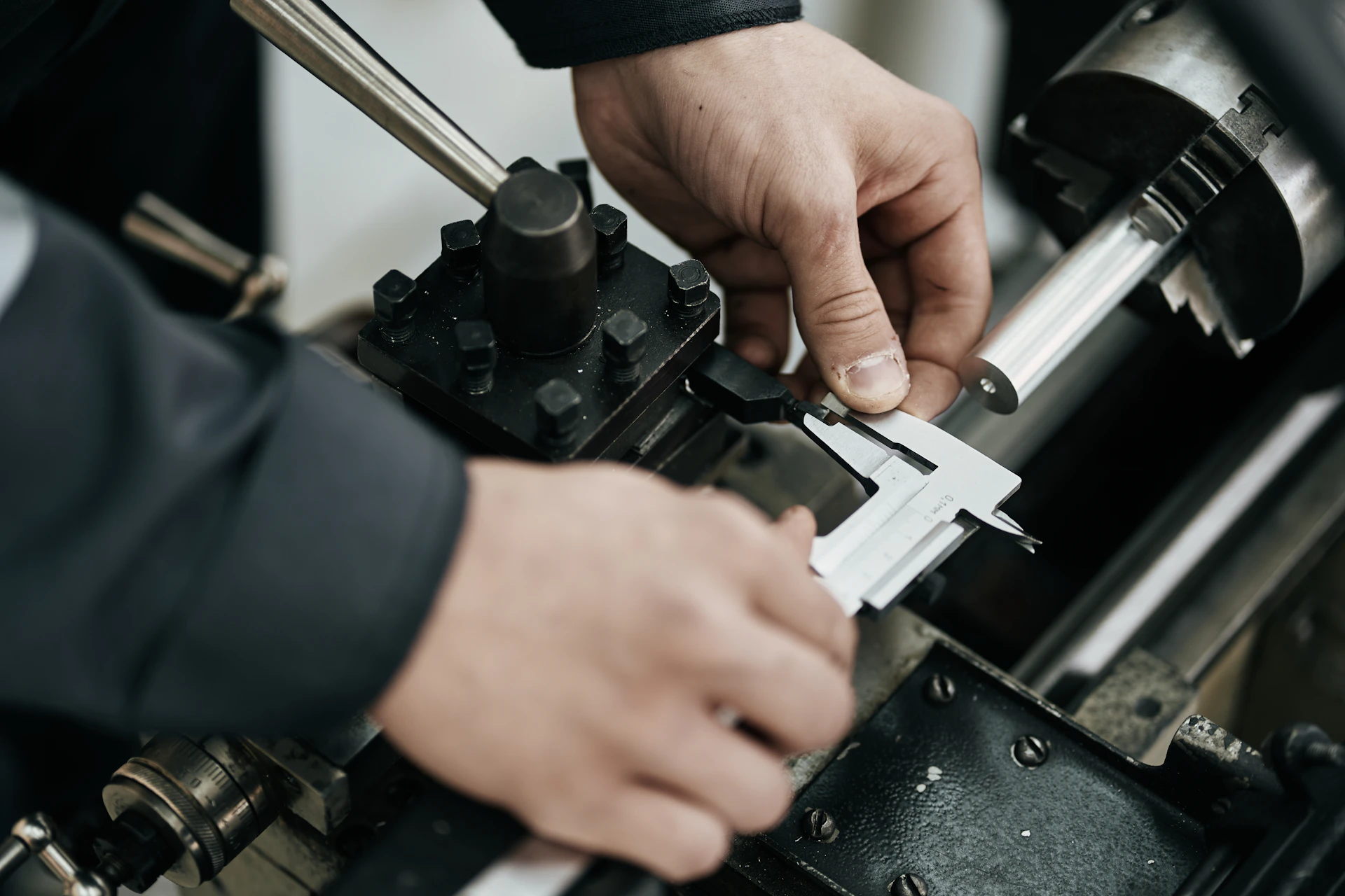 A worker measures a metal rod with calipers.