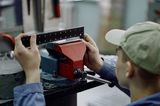A worker measures a metal piece clamped in a vise.