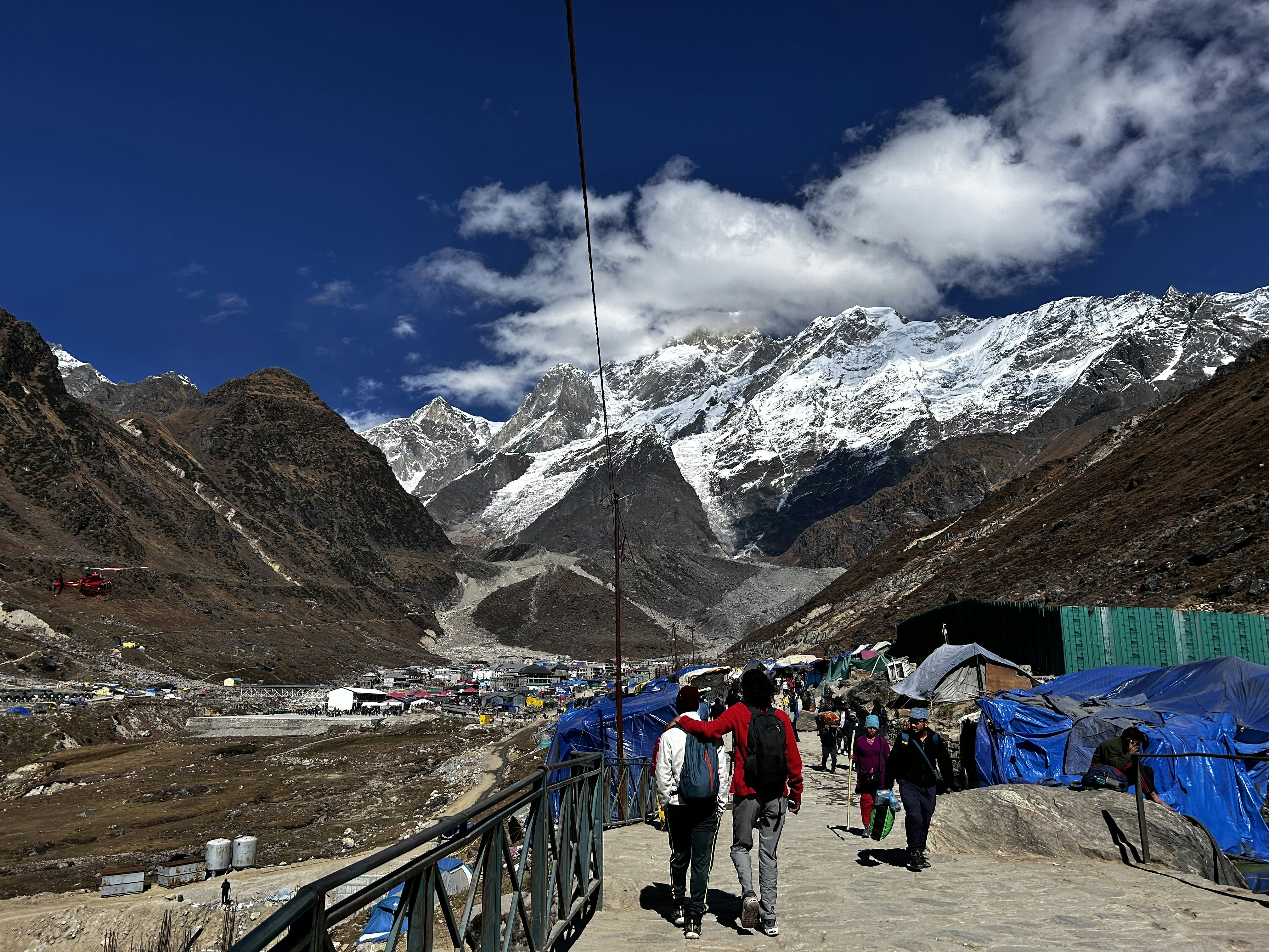 People hike towards snow-capped mountains on a sunny day.