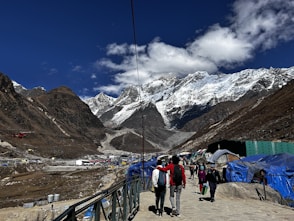 People hike towards snow-capped mountains on a sunny day.