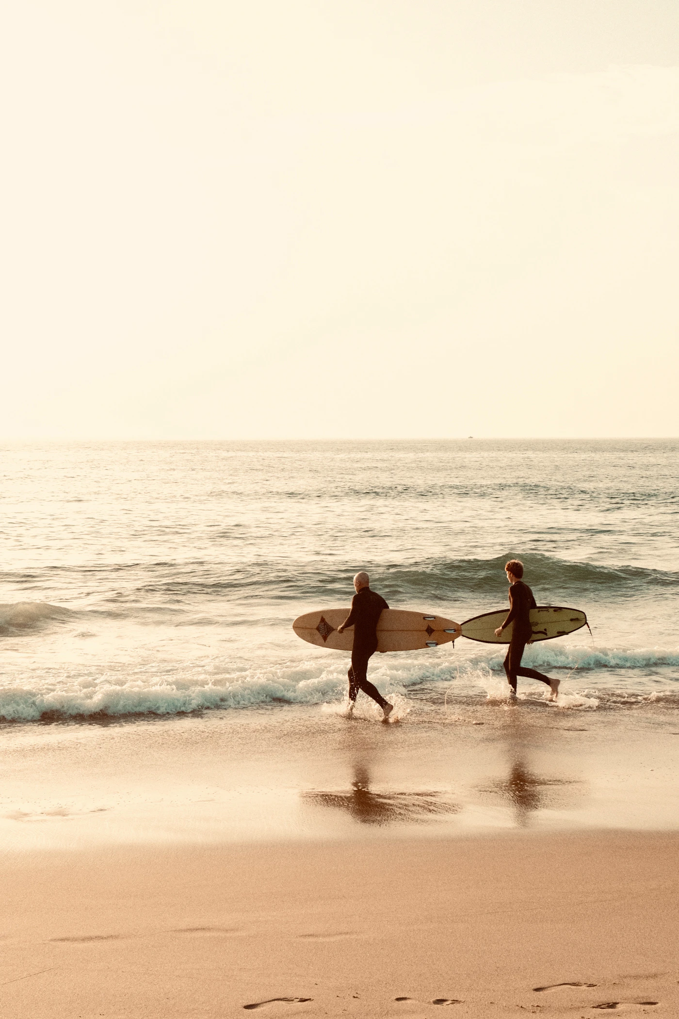 Two surfers walking into the ocean in Lisbon, Portugal