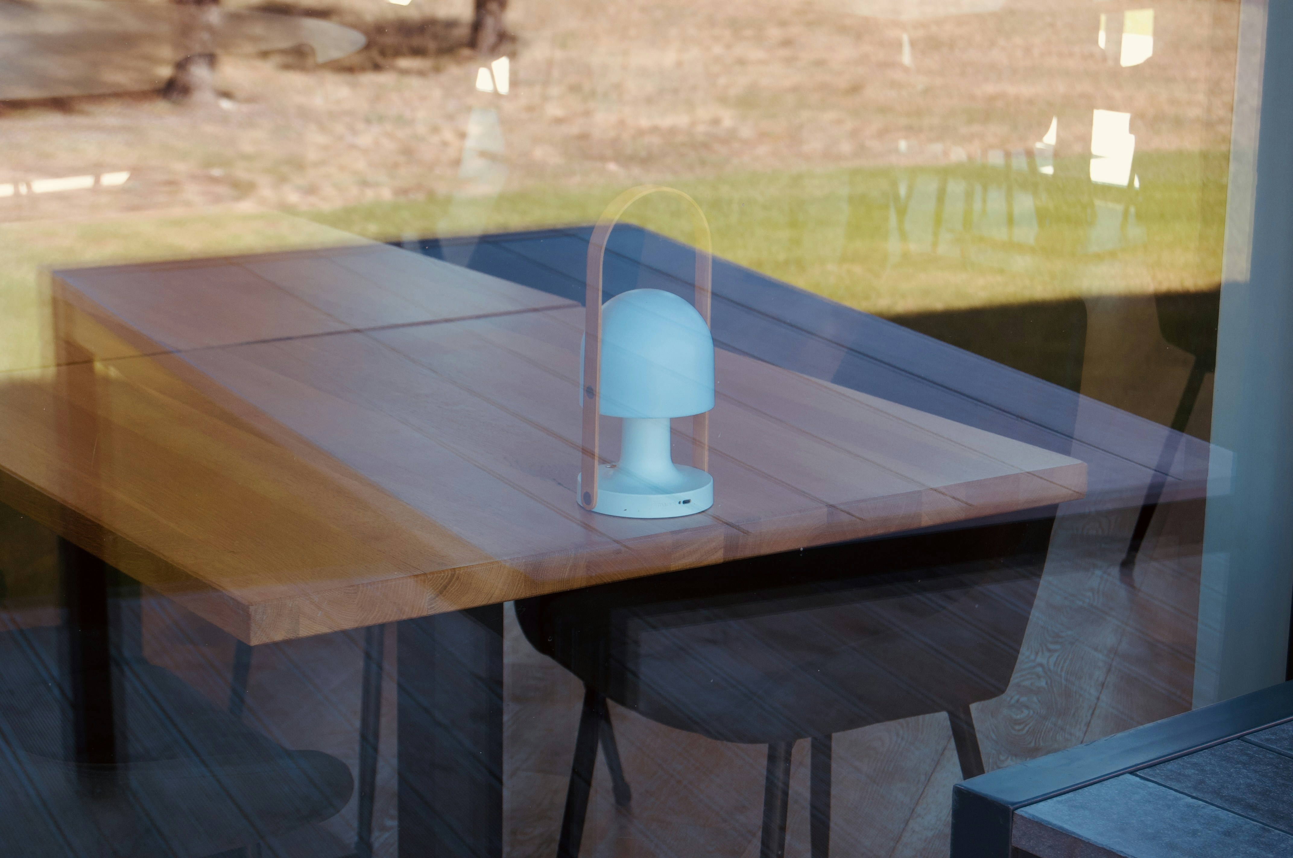 Una lámpara se encuentra sobre una mesa junto a una ventana.