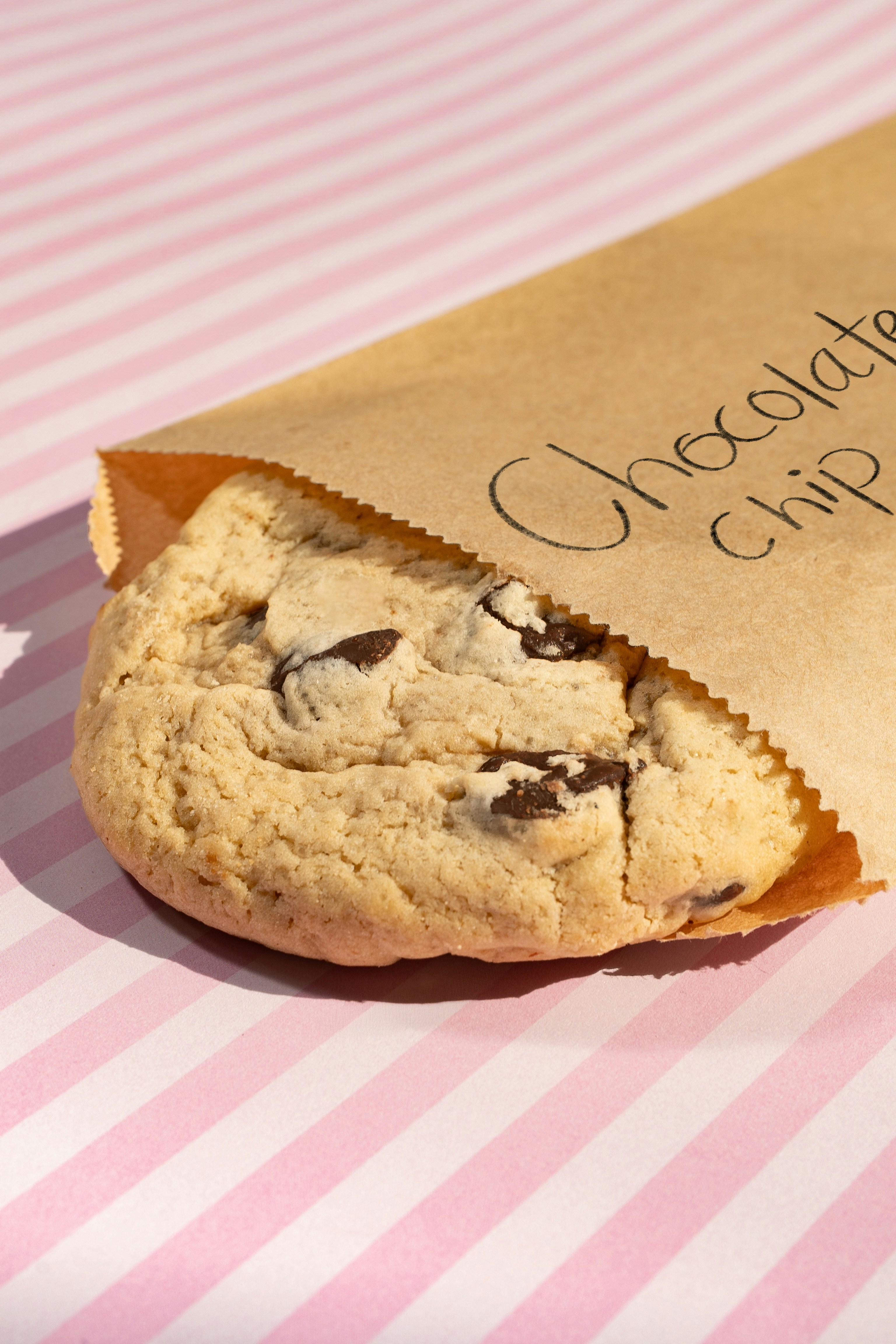 A chocolate chip cookie in a brown paper bag.
