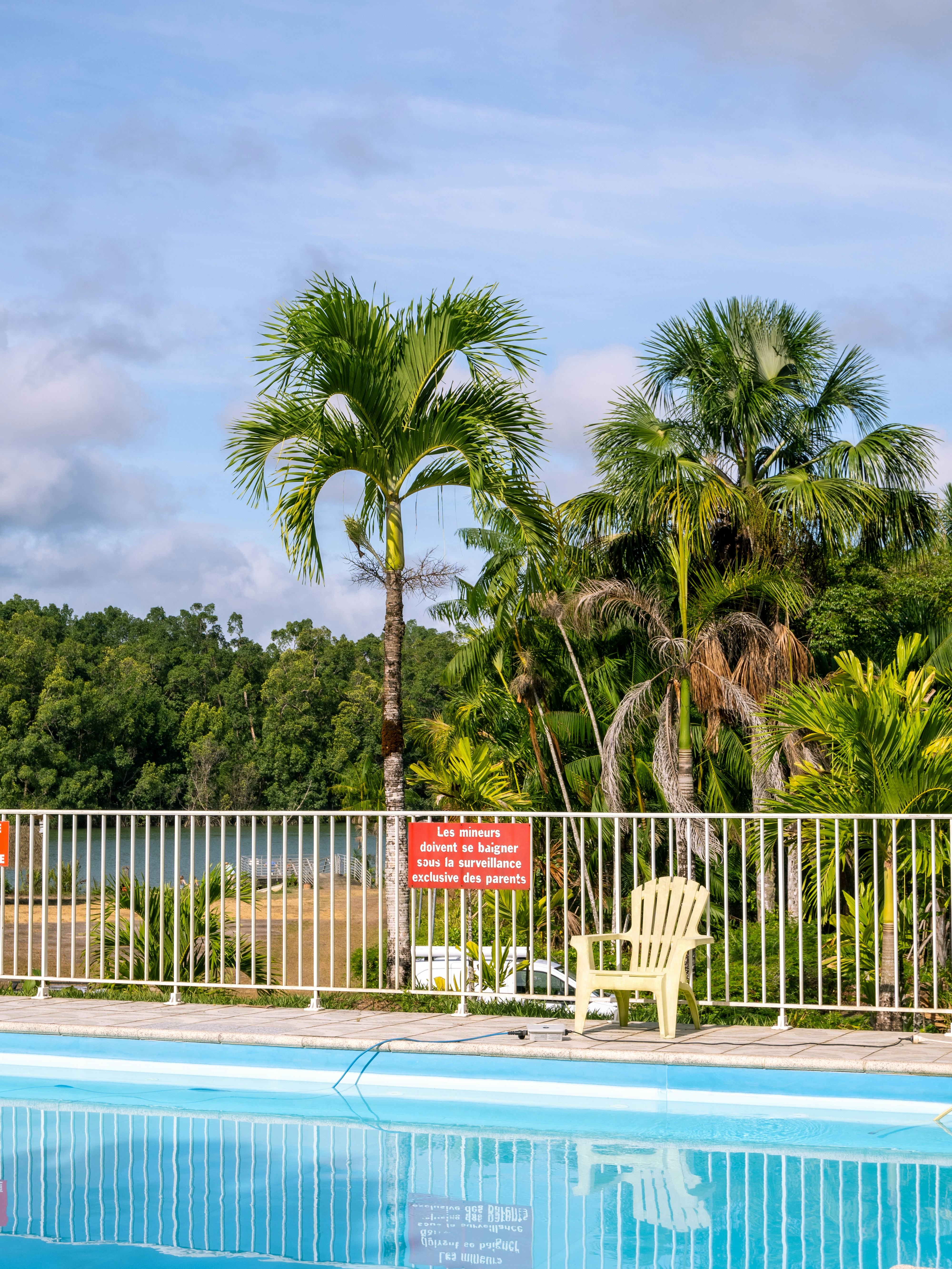 Piscina, alberi e una sedia sotto un cielo luminoso.