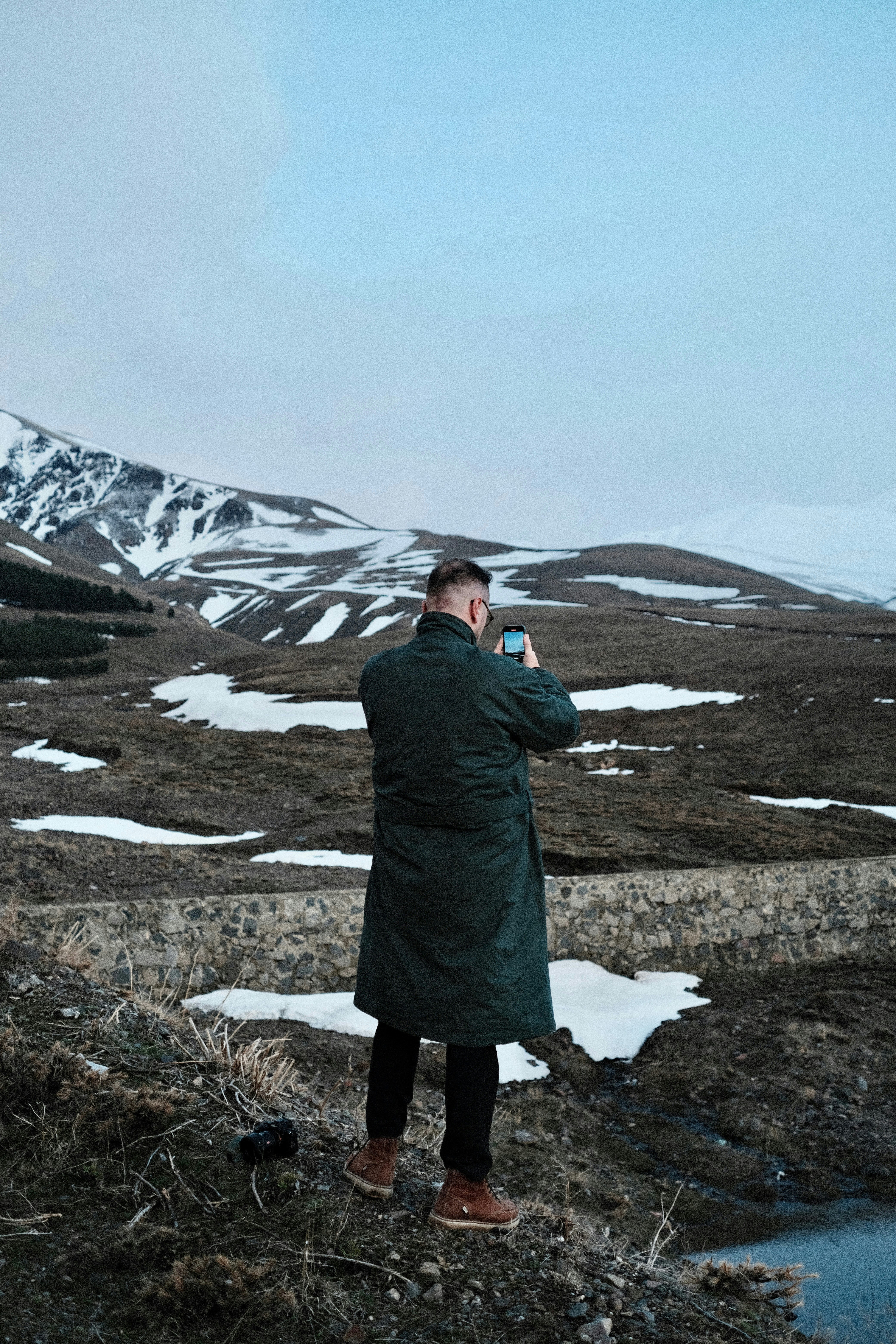 Homem tira uma foto de uma paisagem montanhosa nevada.