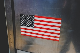 An american flag sticker is displayed on metal.