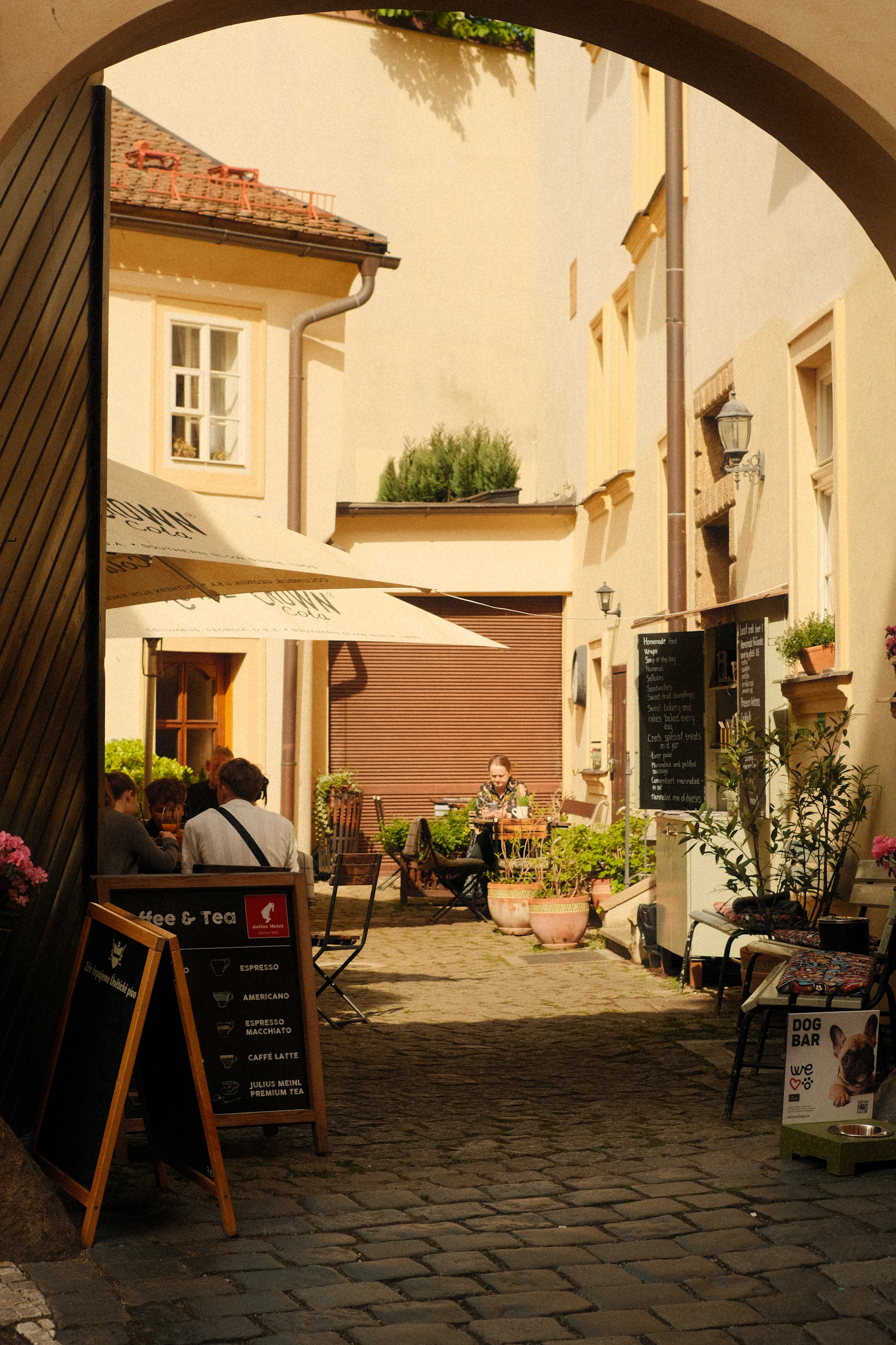 A small café courtyard framed by a stone archway in Prague