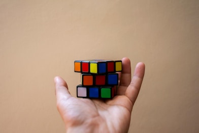 A hand holds a colorful, unsolved rubik's cube.
