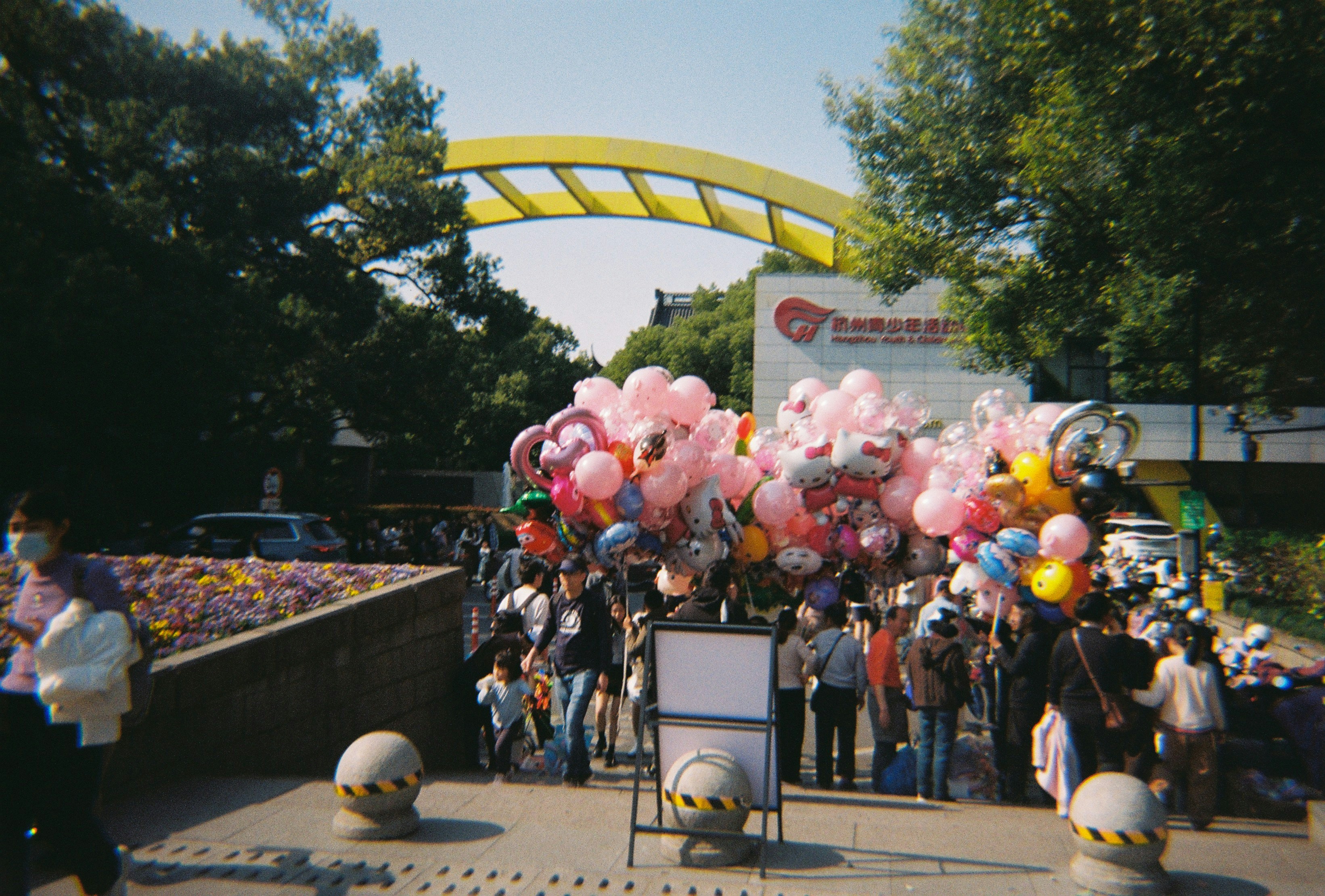 People are gathering with balloons near a yellow arch.