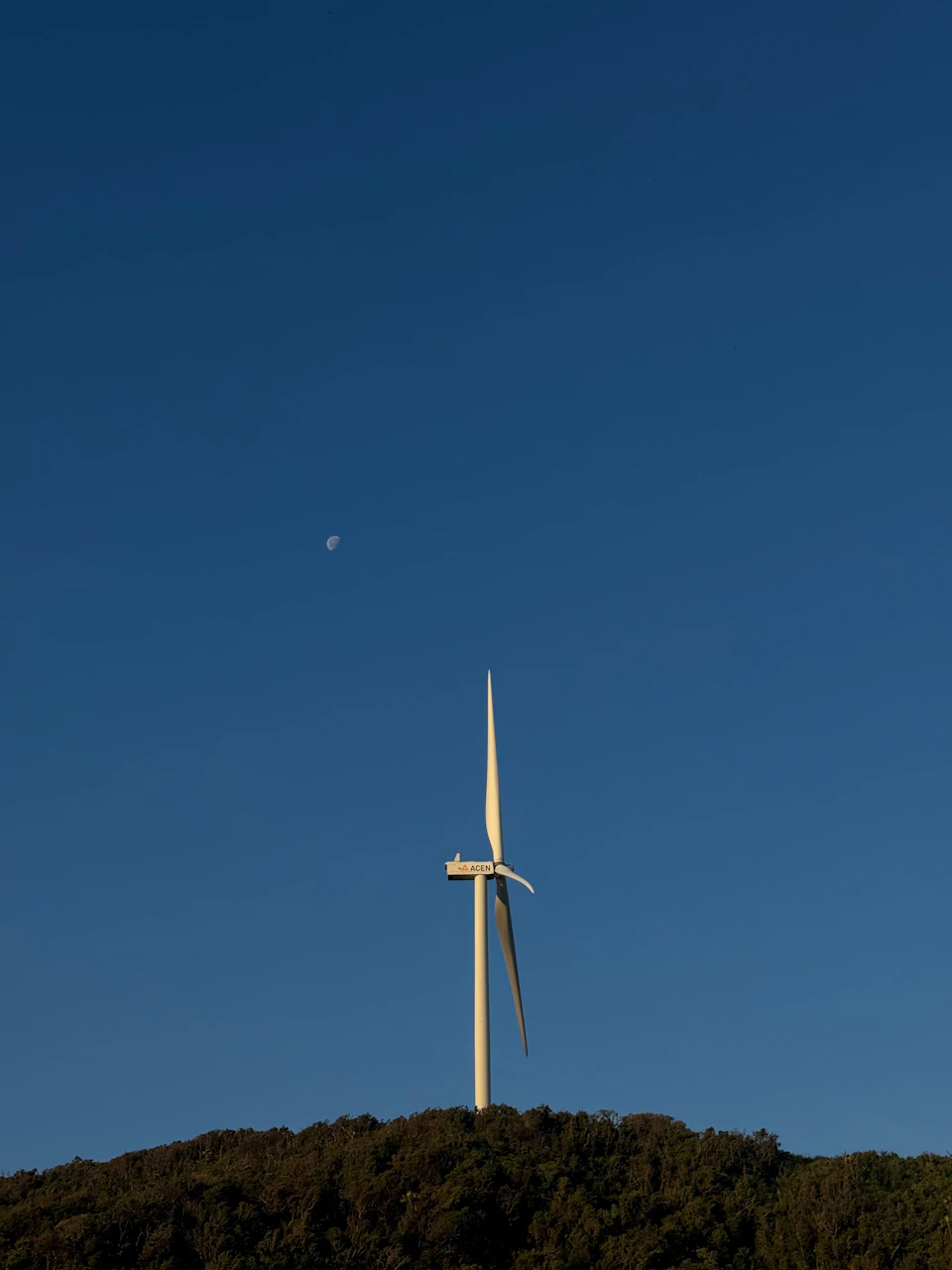 Large white wind turbine stands tall on a hill with its blades facing right