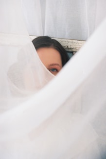 A woman peeks out from behind fabric.
