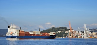 A cargo ship sails near a busy harbor.