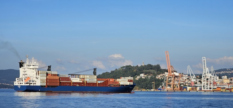 A cargo ship sails near a busy harbor.
