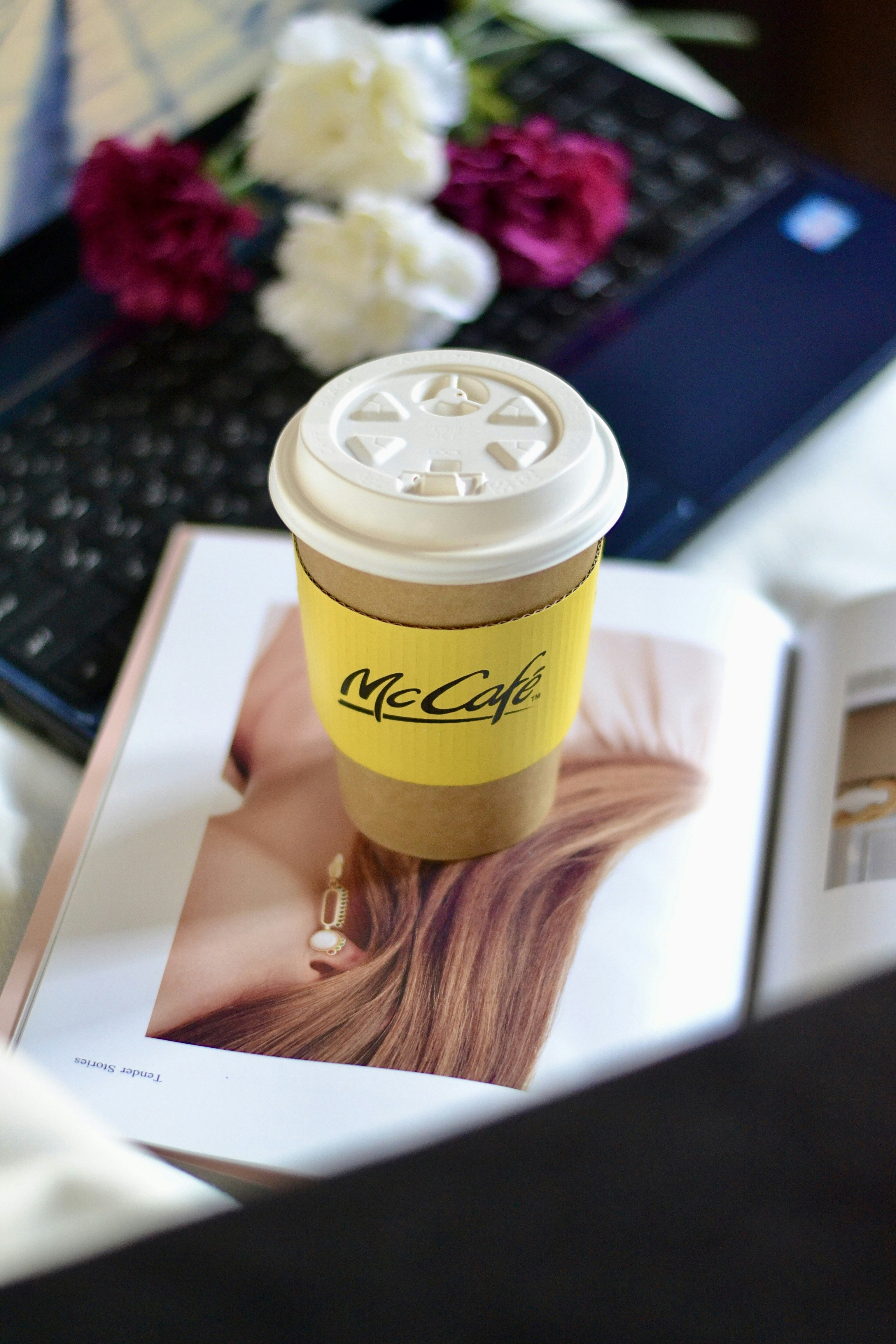 花とラップトップのある雑誌の上のコーヒーカップ。