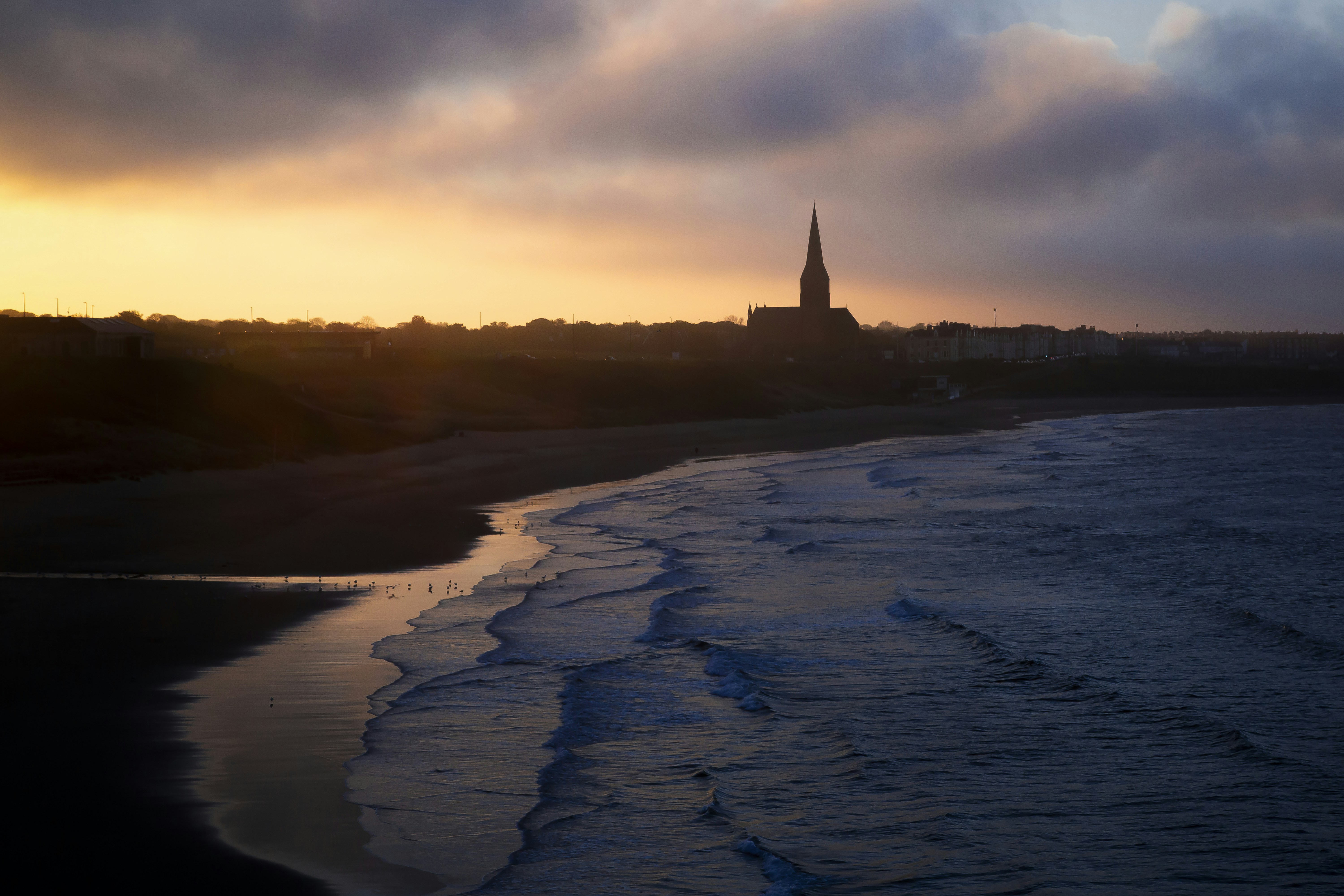 Sunset bathes a church silhouette over the ocean.