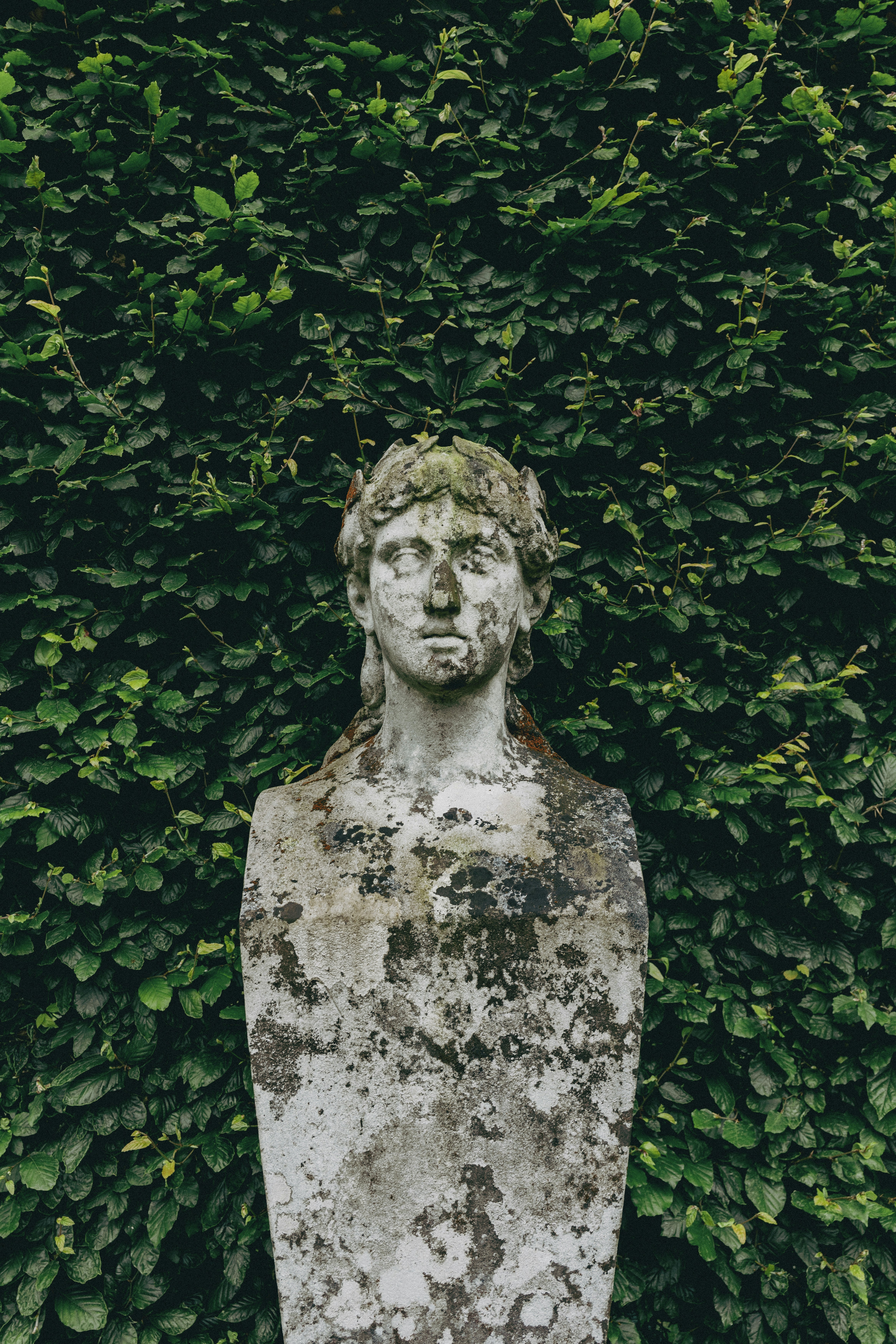 A weathered statue stands against a green wall.