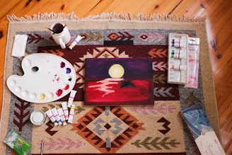 DIY crafts, art supplies surround a finished painting of a landscape.