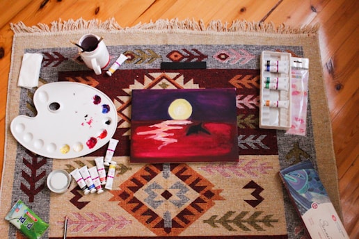 DIY crafts, art supplies surround a finished painting of a landscape.