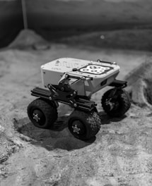 A robotic rover explores a desolate, lunar-like surface.