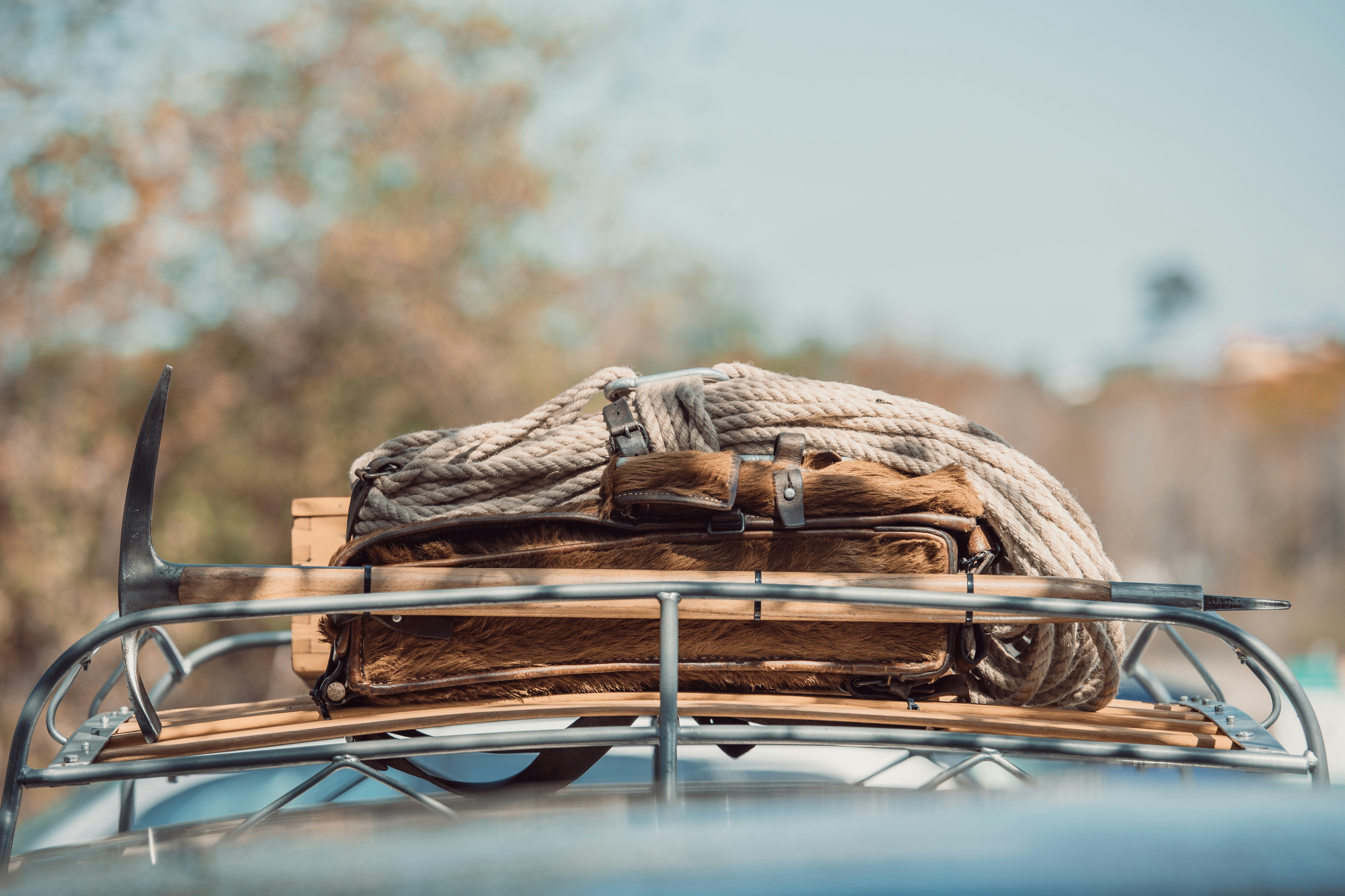 Vintage-style roof basket on a car carrying a leather bag, a coil of rope and a wooden crate, with an ice axe lashed along one side