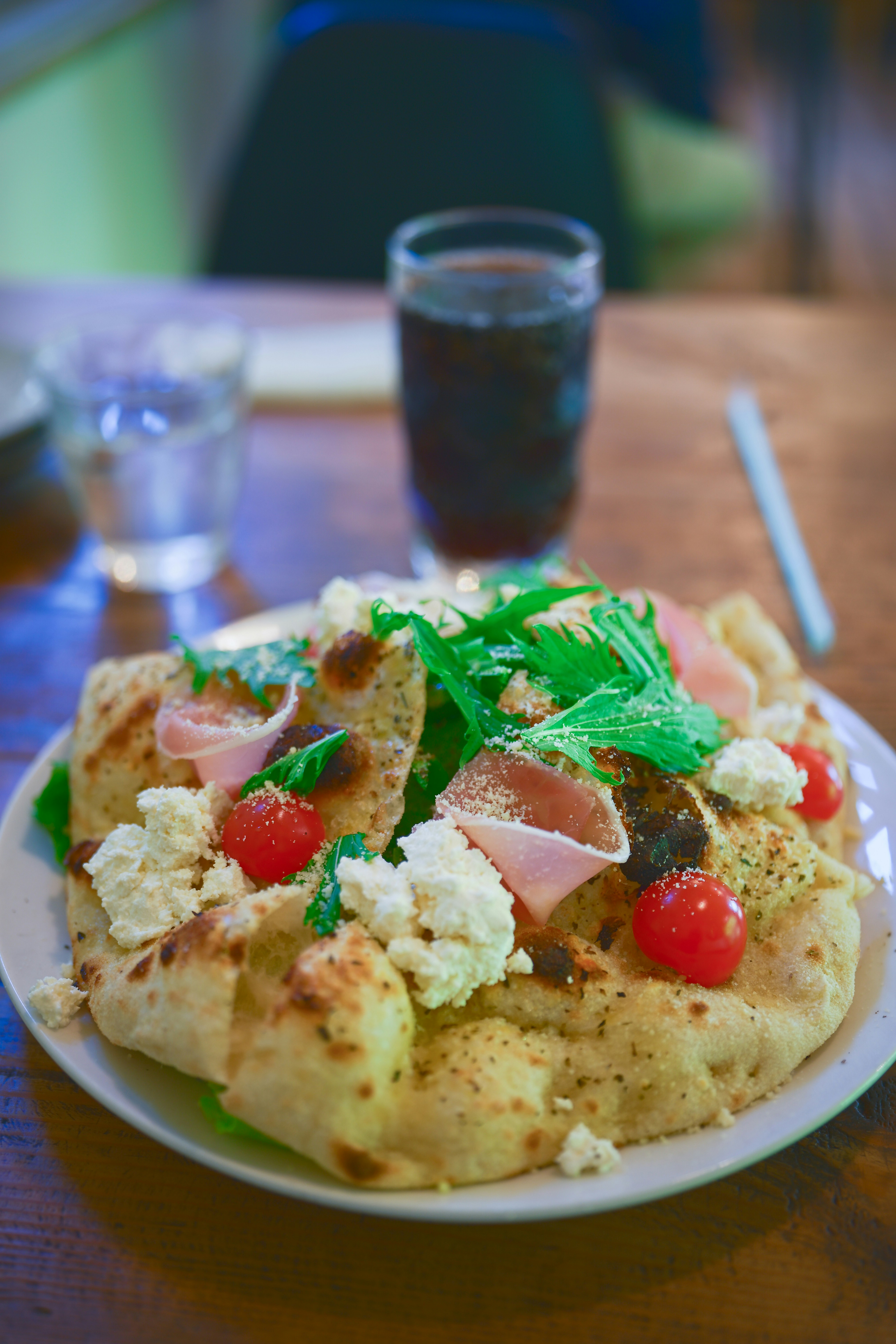 Pizza garnie de tomates, de prosciutto et de légumes verts.