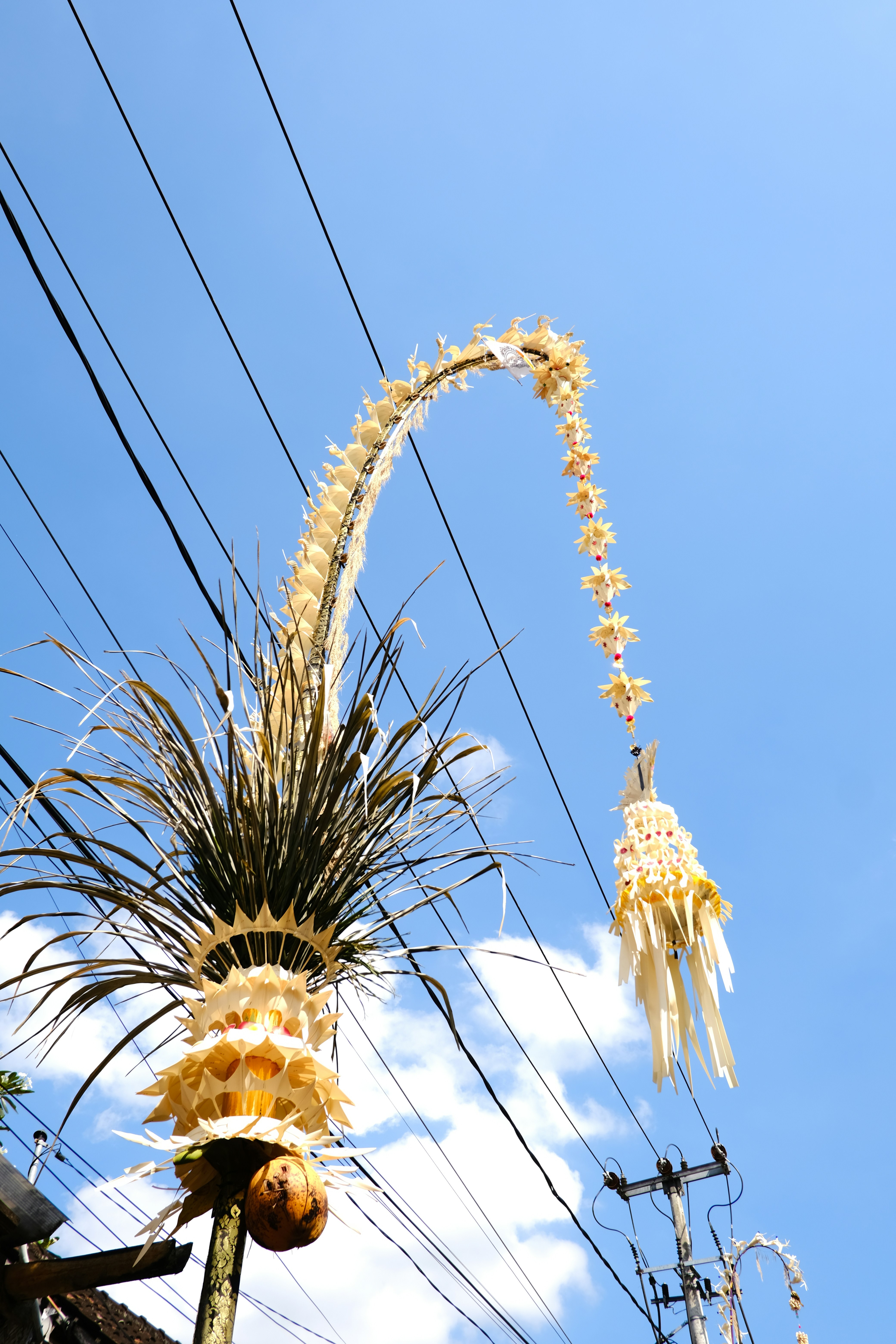 A balinese penjor adorns the blue sky.