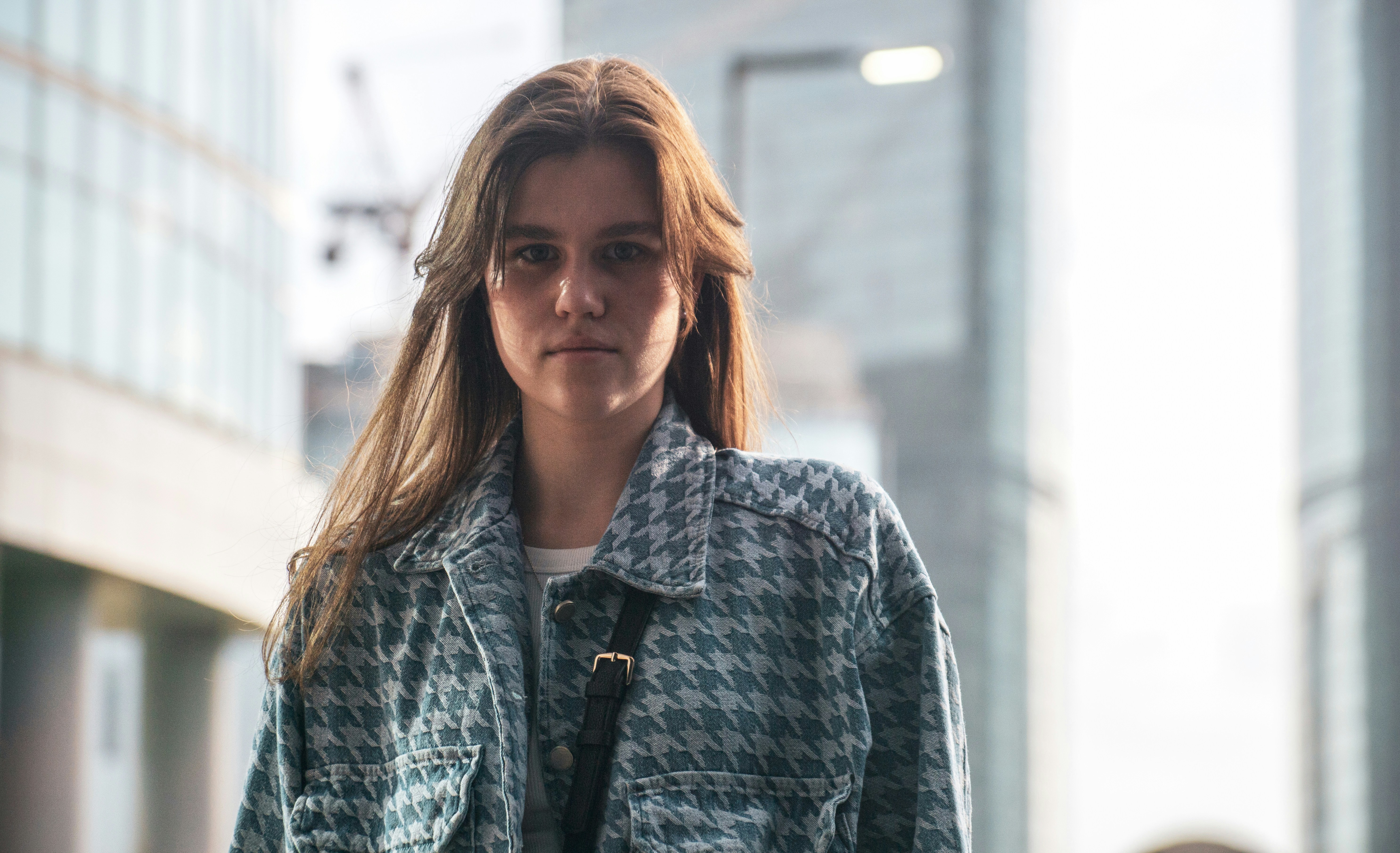 A young woman poses in front of city buildings.