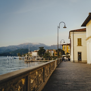 A lakeside promenade with buildings and mountains.