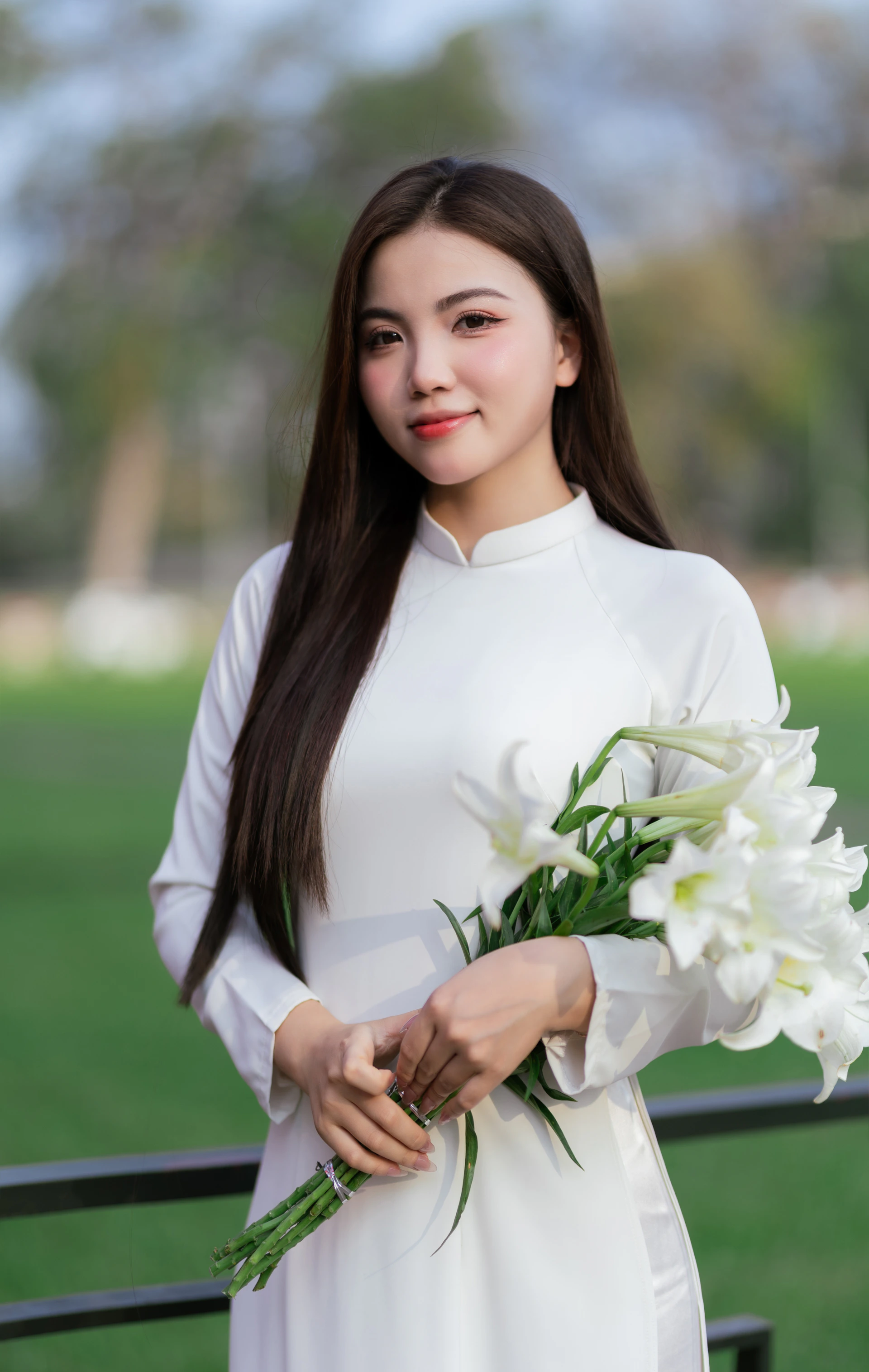A woman holds lilies, wearing a white dress.