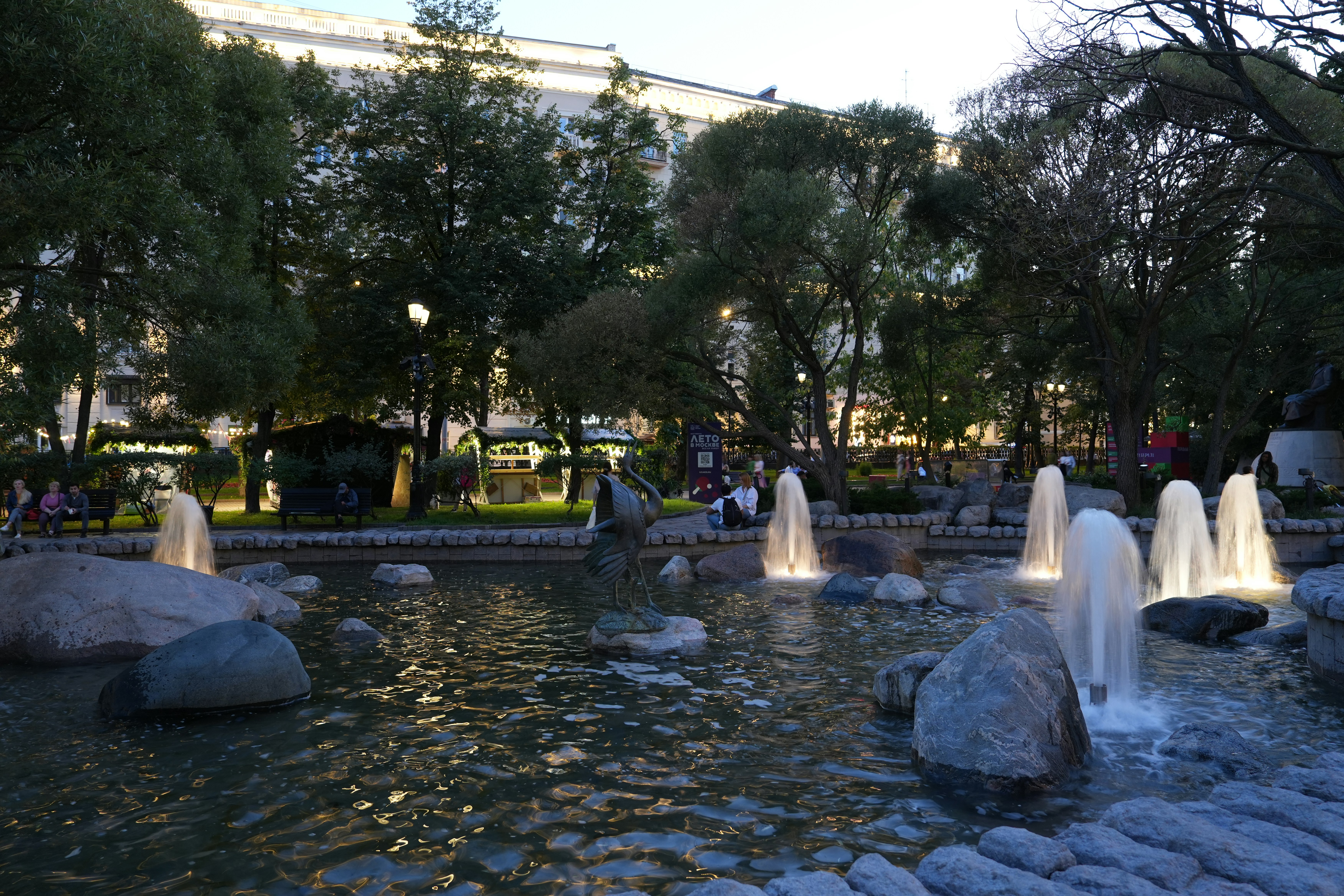 A fountain in a park glows at dusk.