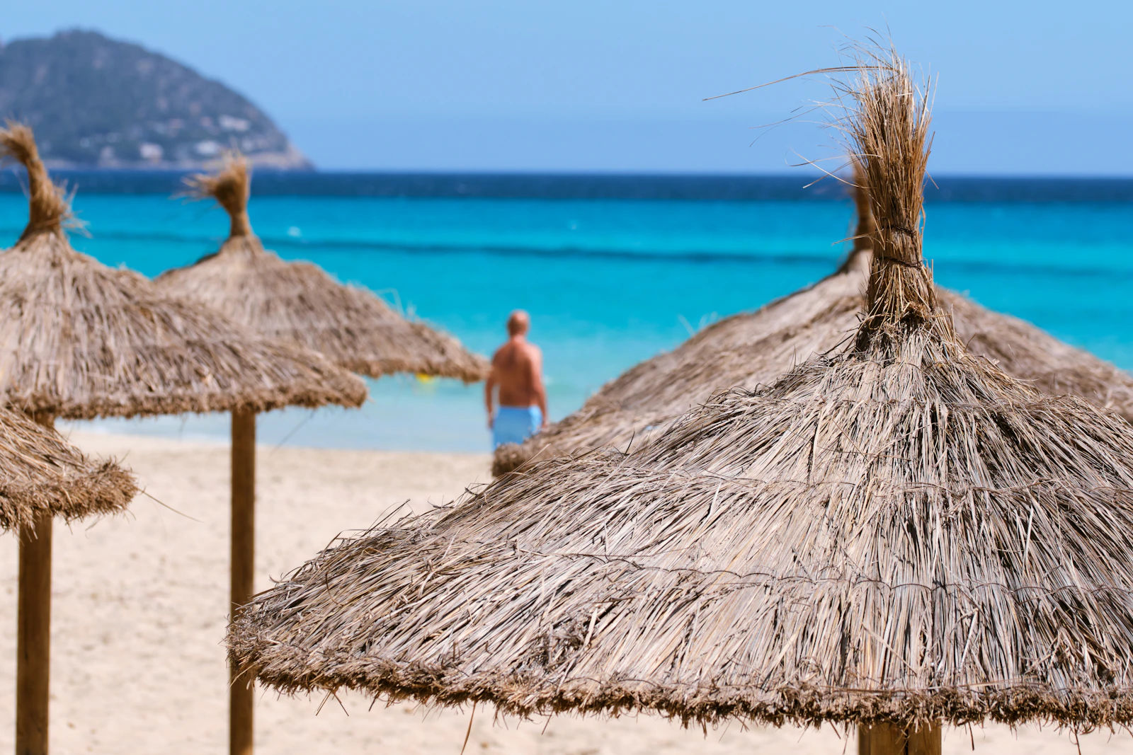 Straw beach parasols beside clear turquoise water in Mallorca