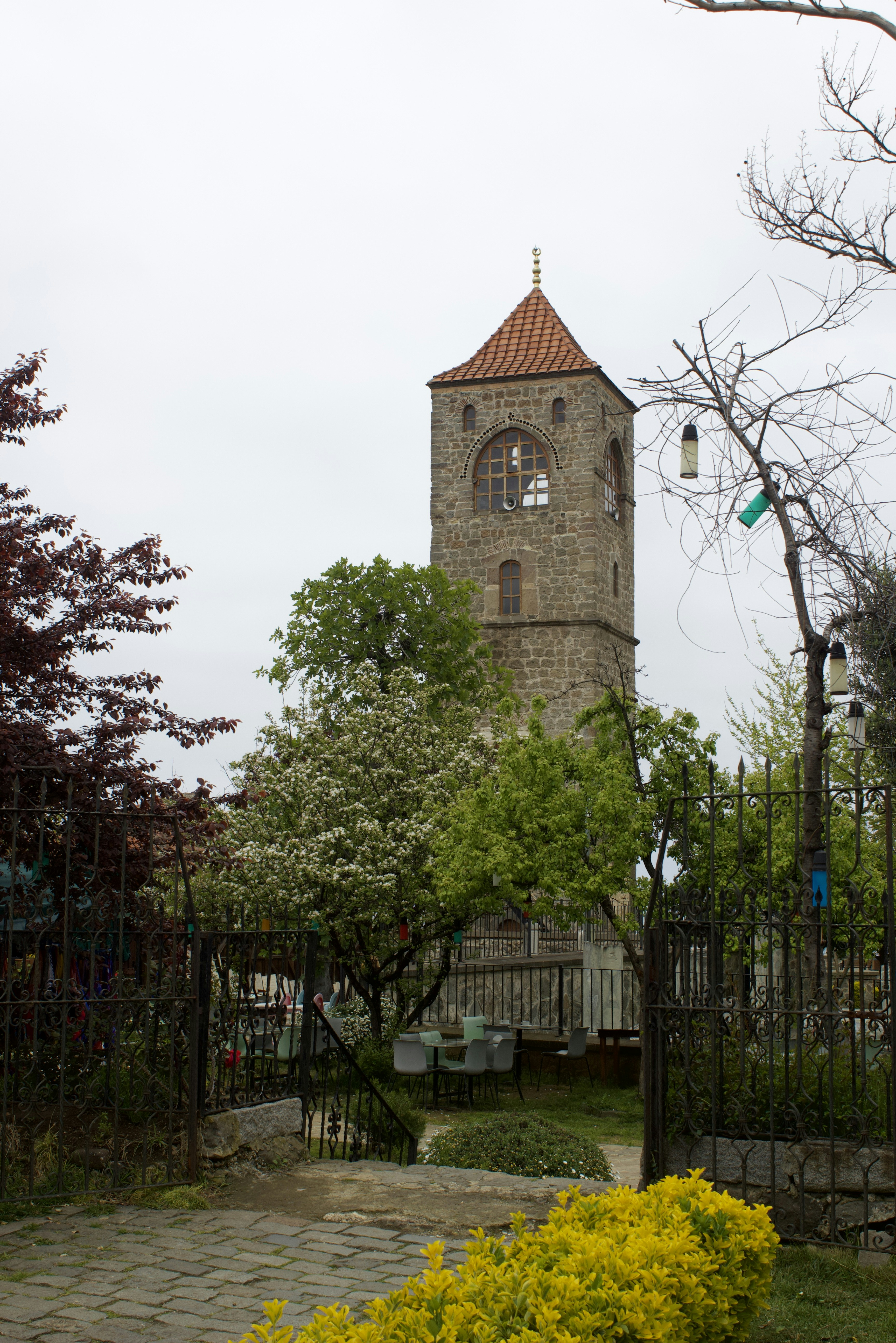 A tall stone tower stands near lush greenery.
