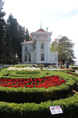 A white building stands near a beautiful flower garden.