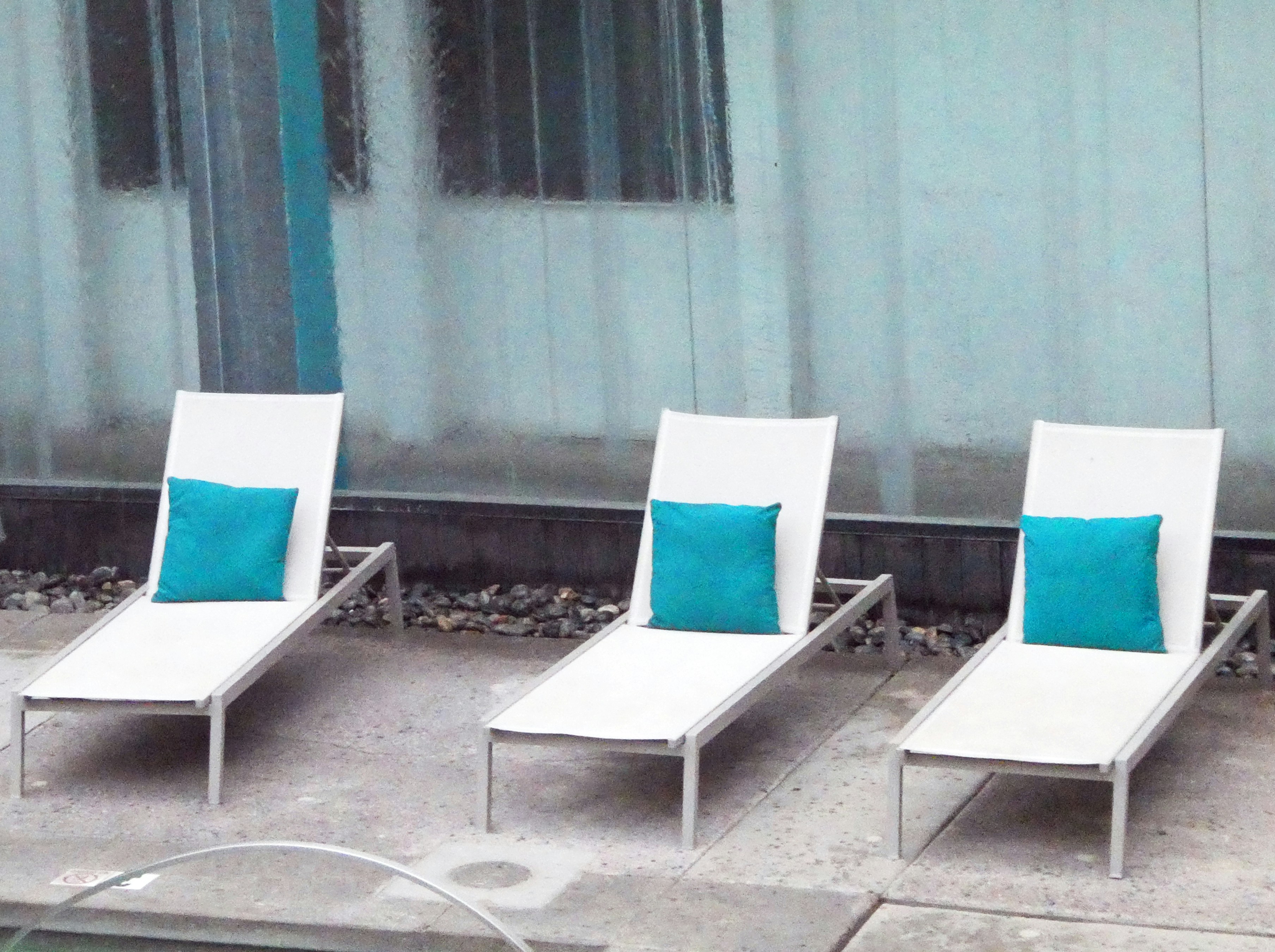 Three lounge chairs sit poolside with pillows.