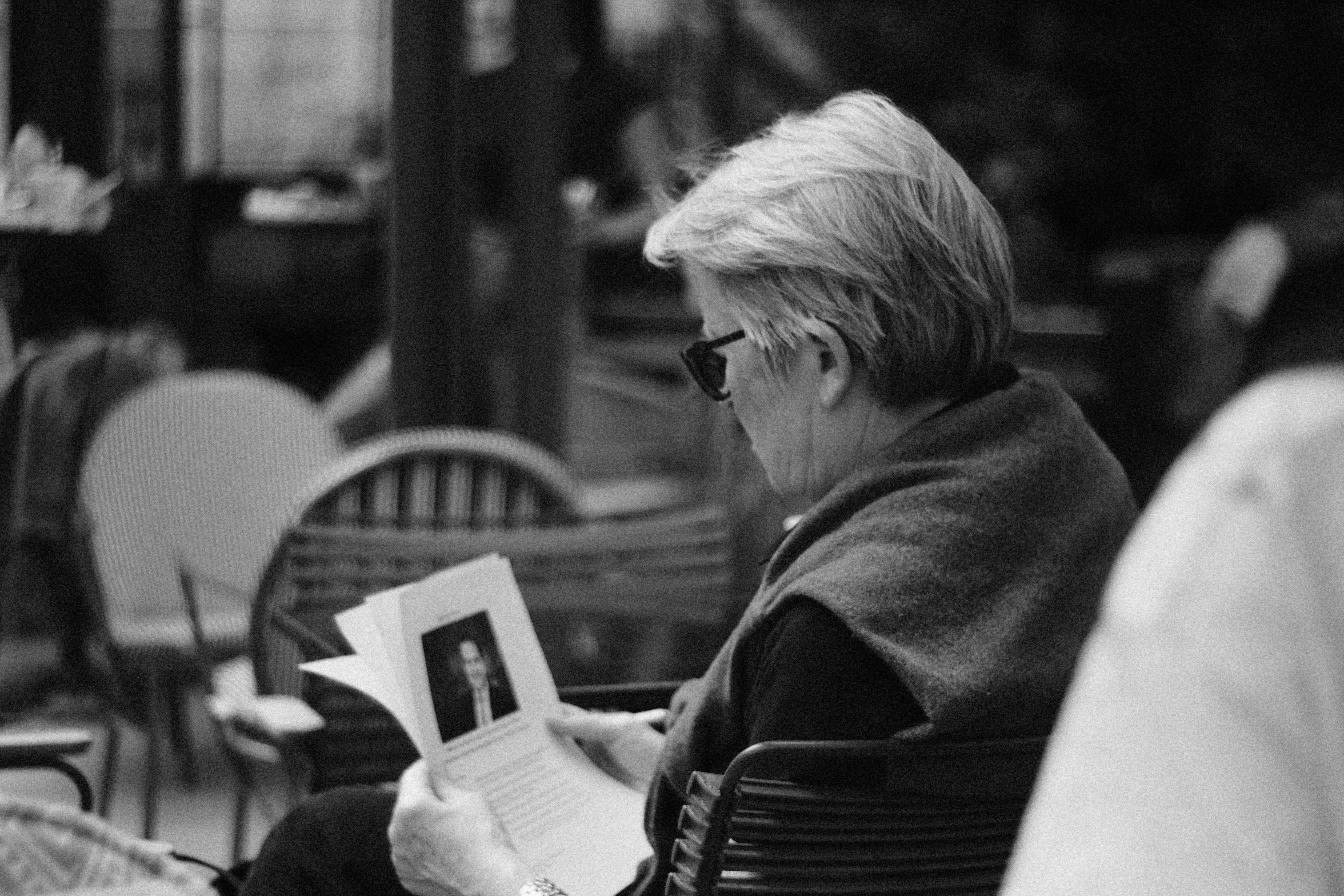 An elderly woman reads a book outdoors.