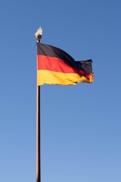The german flag is waving against a blue sky.