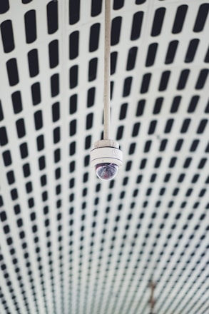 A security camera hangs from a patterned ceiling.